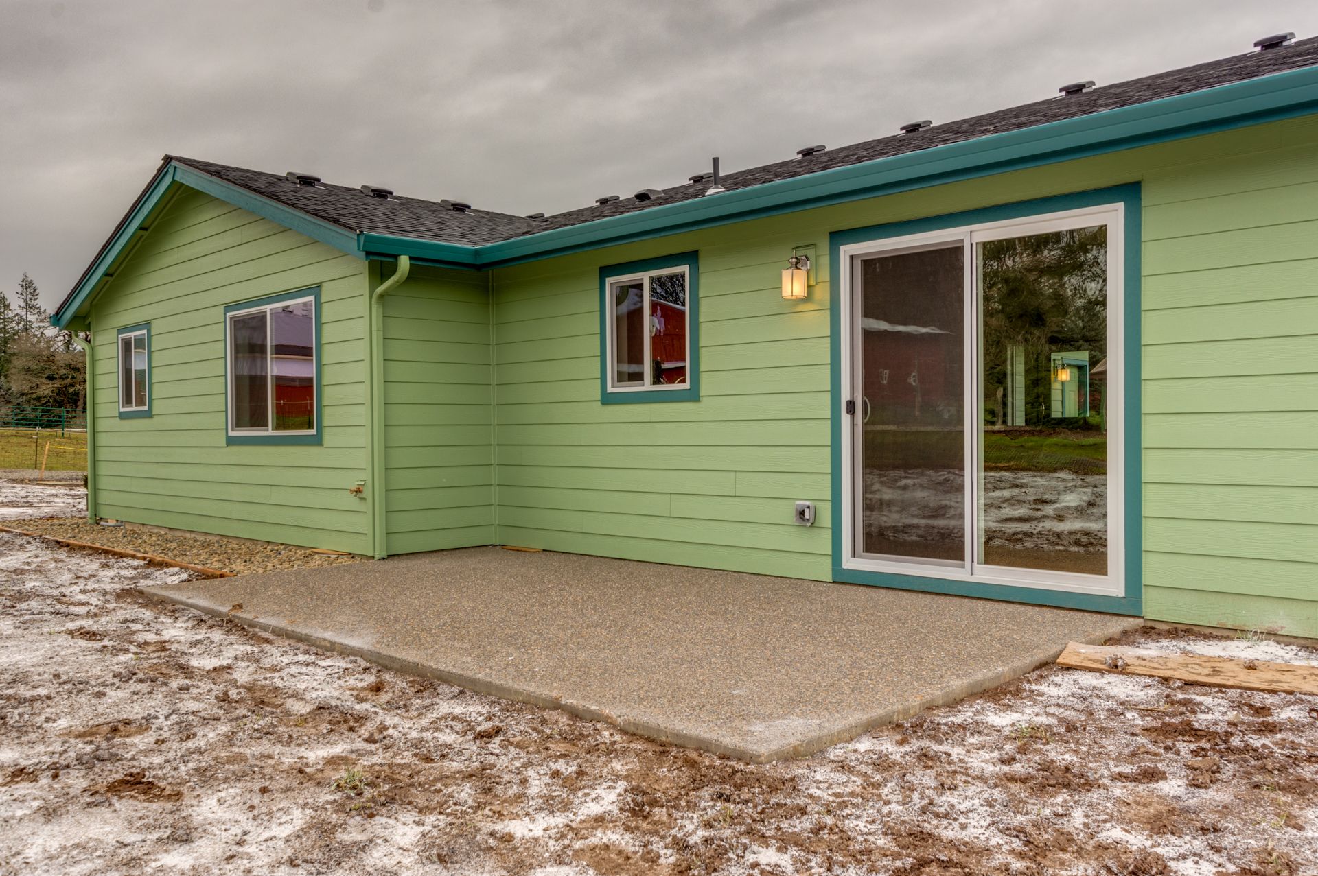 The back of a green house with a patio and sliding glass doors.