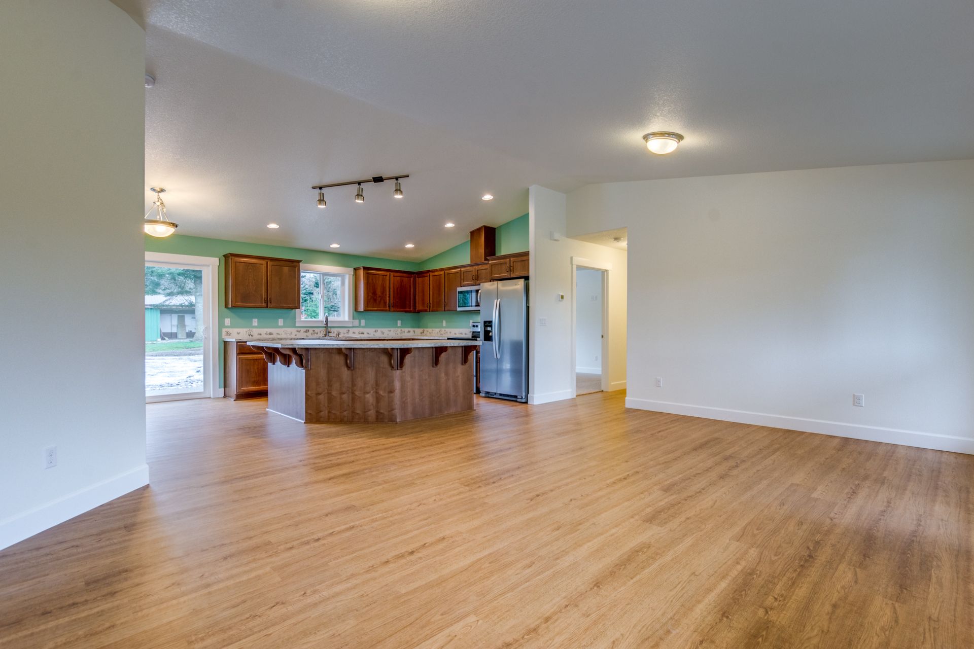 An empty living room with hardwood floors and a kitchen in the background.