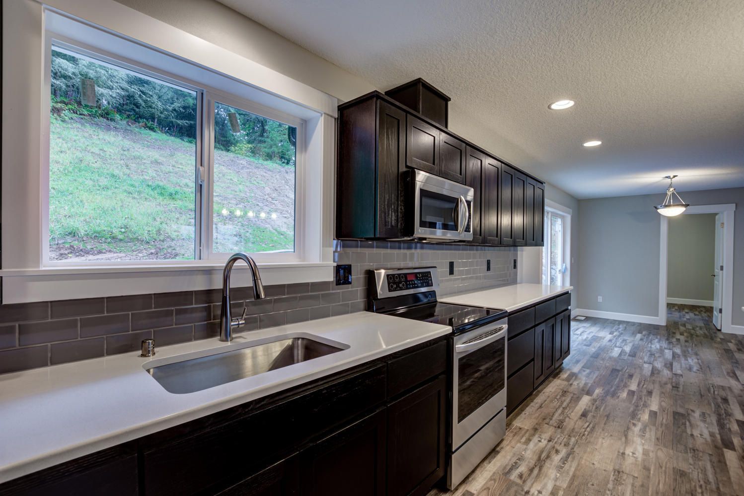 A kitchen with a sink , stove , microwave , and two windows.