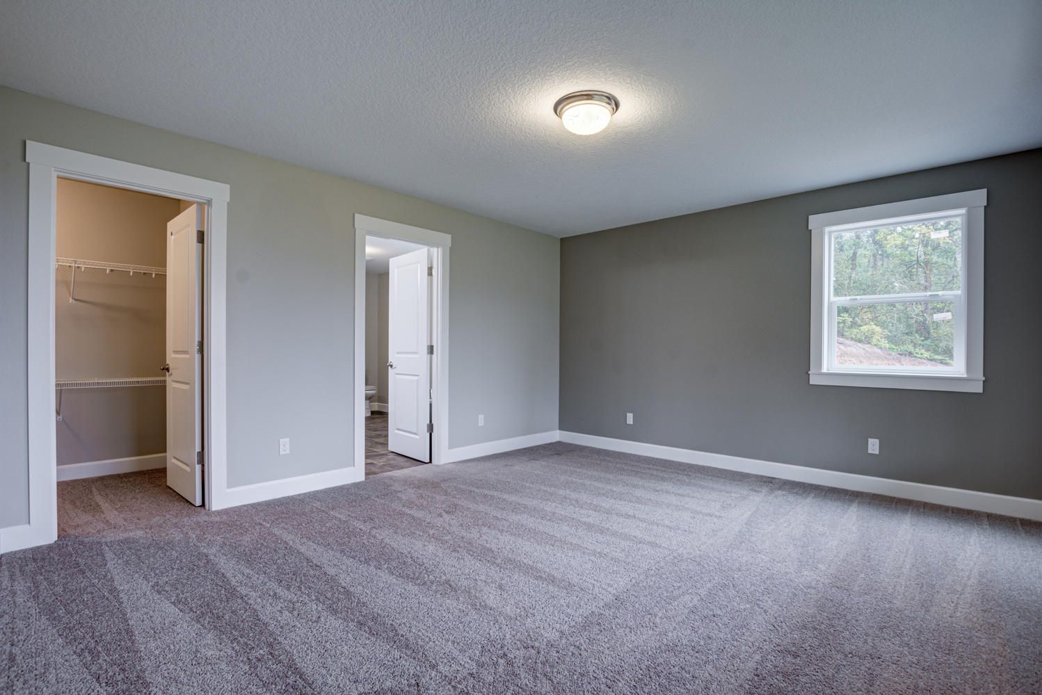 An empty bedroom with a carpeted floor and a window.