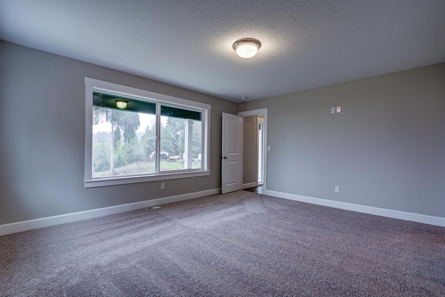 An empty room with a large window and a carpeted floor.