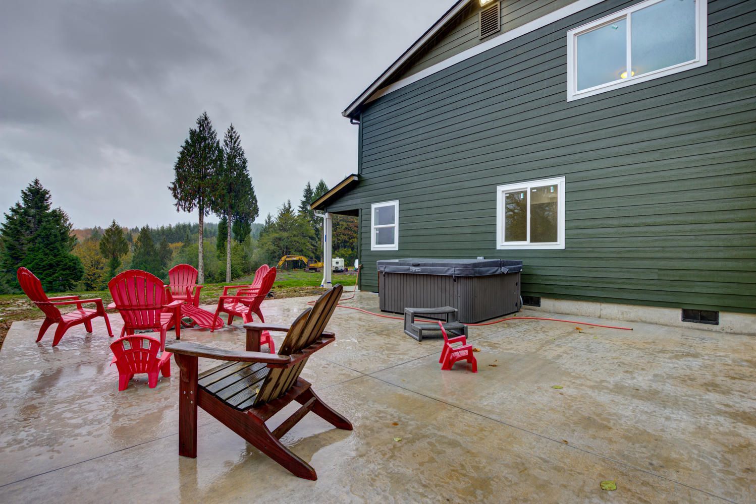 A patio with red chairs and a hot tub in front of a green house.