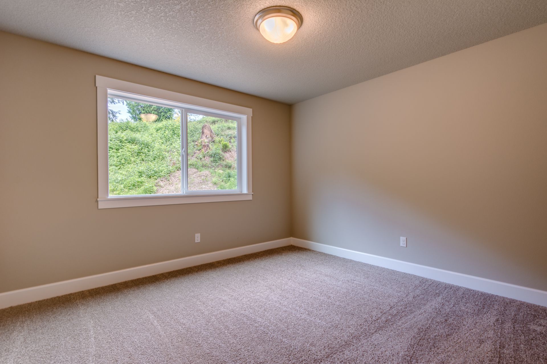 An empty bedroom with a window and a ceiling light.