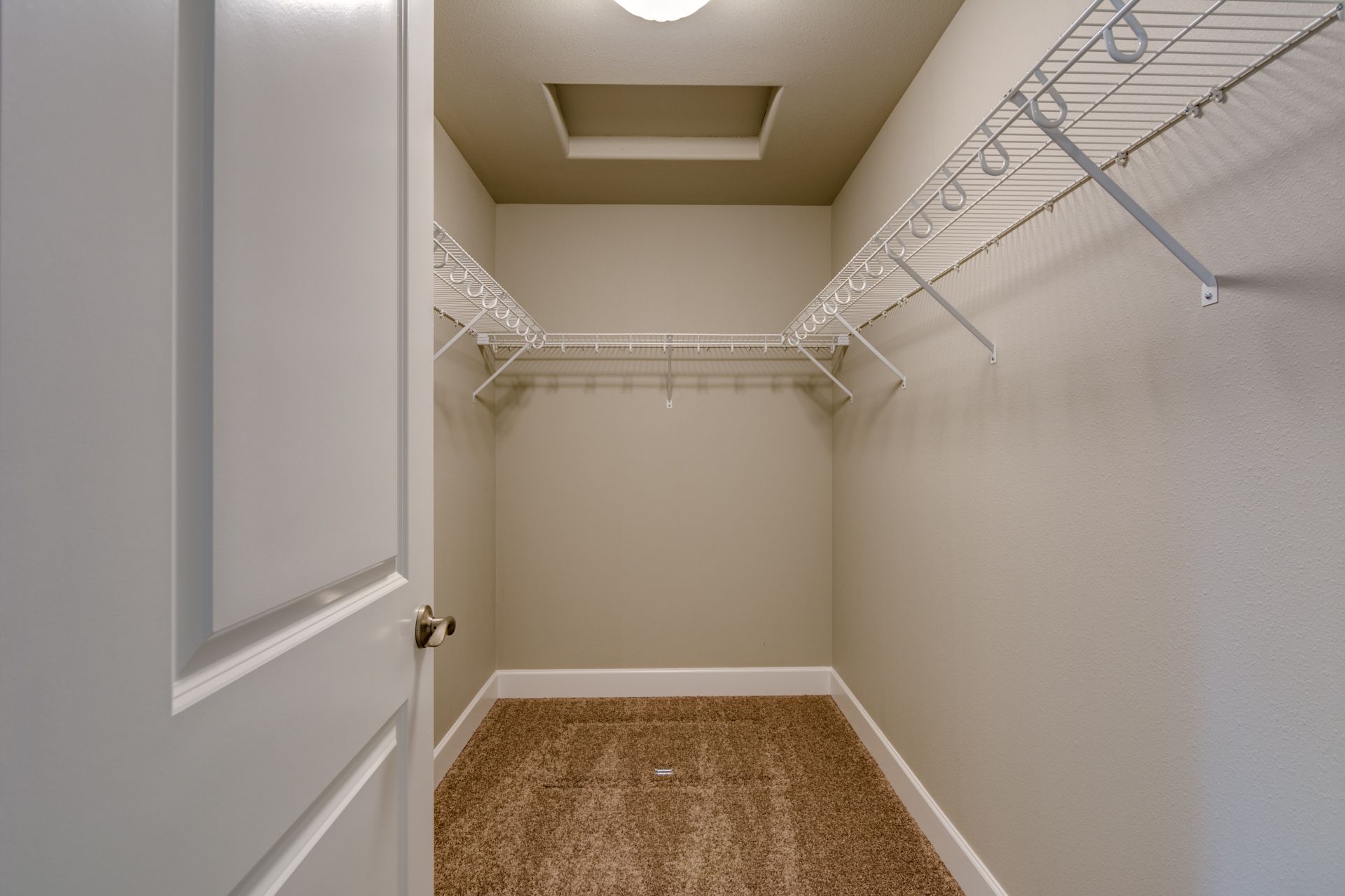 An empty walk in closet with a white door and a ceiling light.