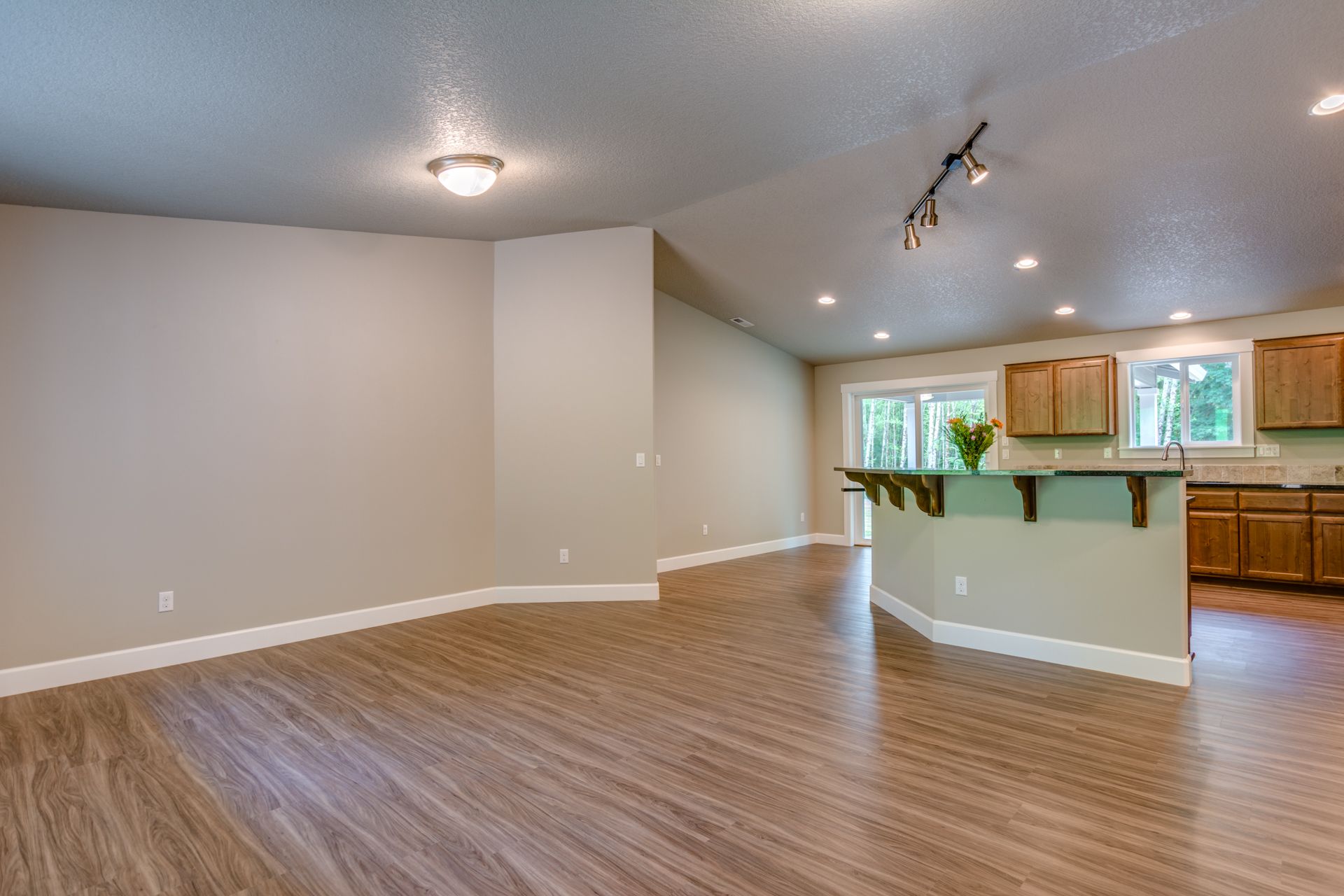 An empty living room with hardwood floors and a kitchen in the background.