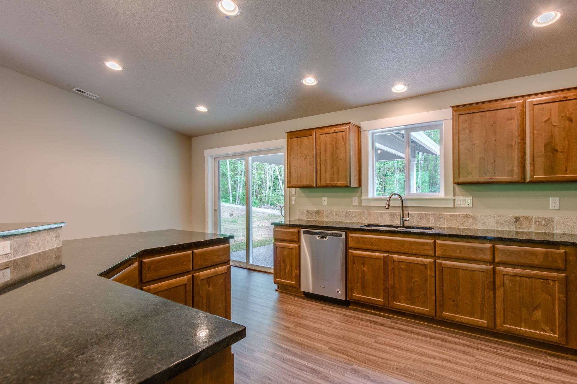 A kitchen with wooden cabinets , granite counter tops , a sink , and a sliding glass door.