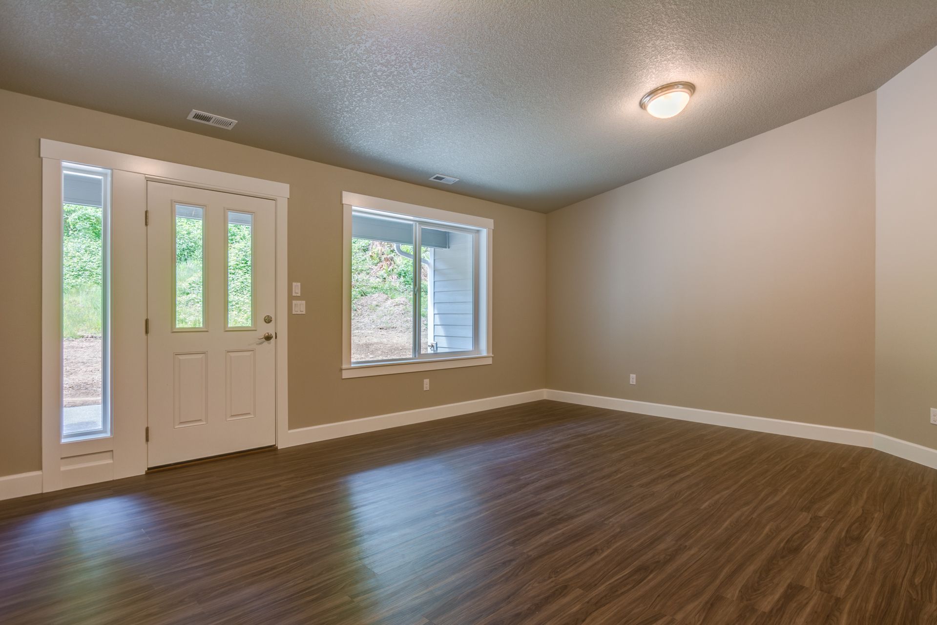 An empty living room with hardwood floors and two windows.