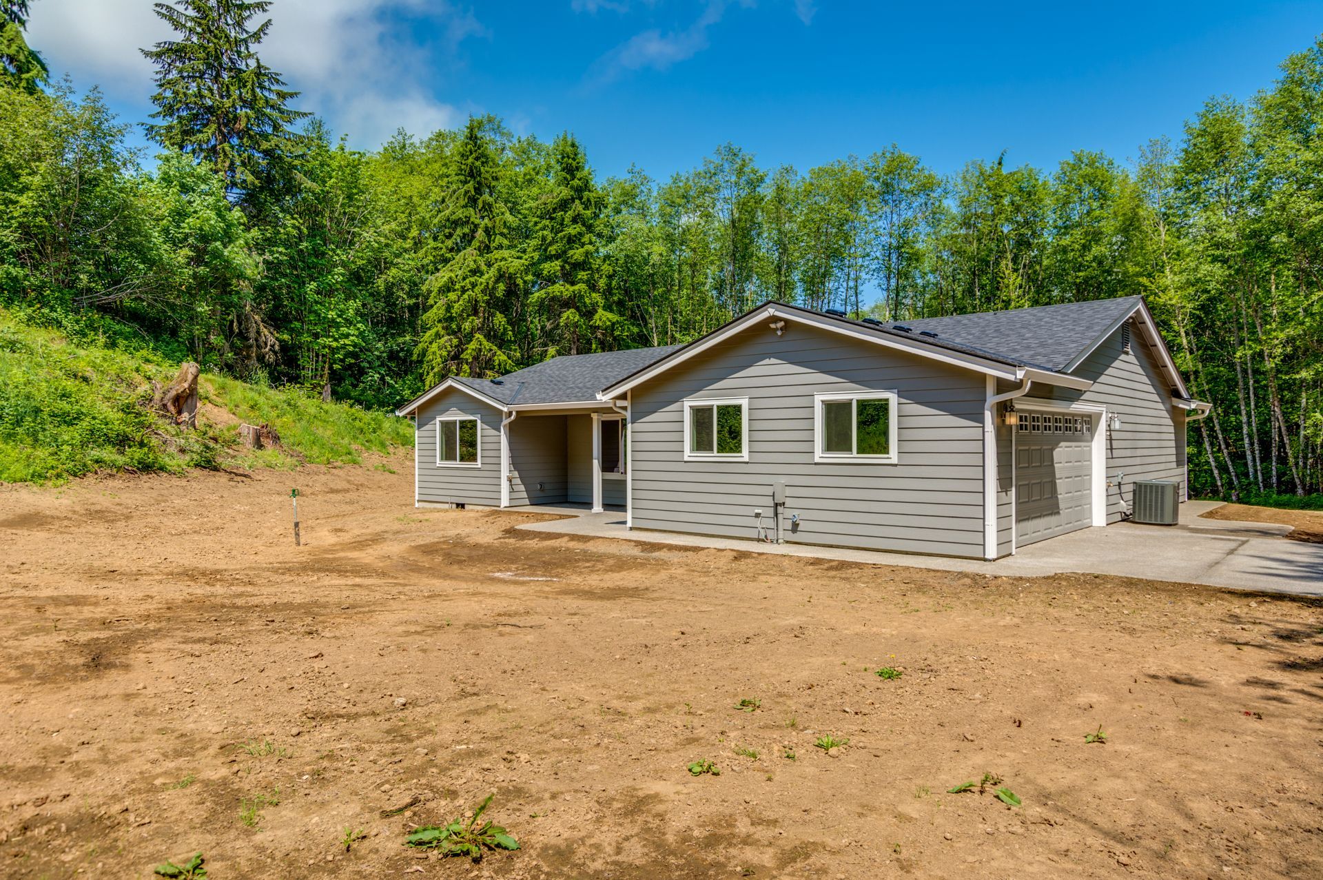 A house is sitting in the middle of a dirt field surrounded by trees.