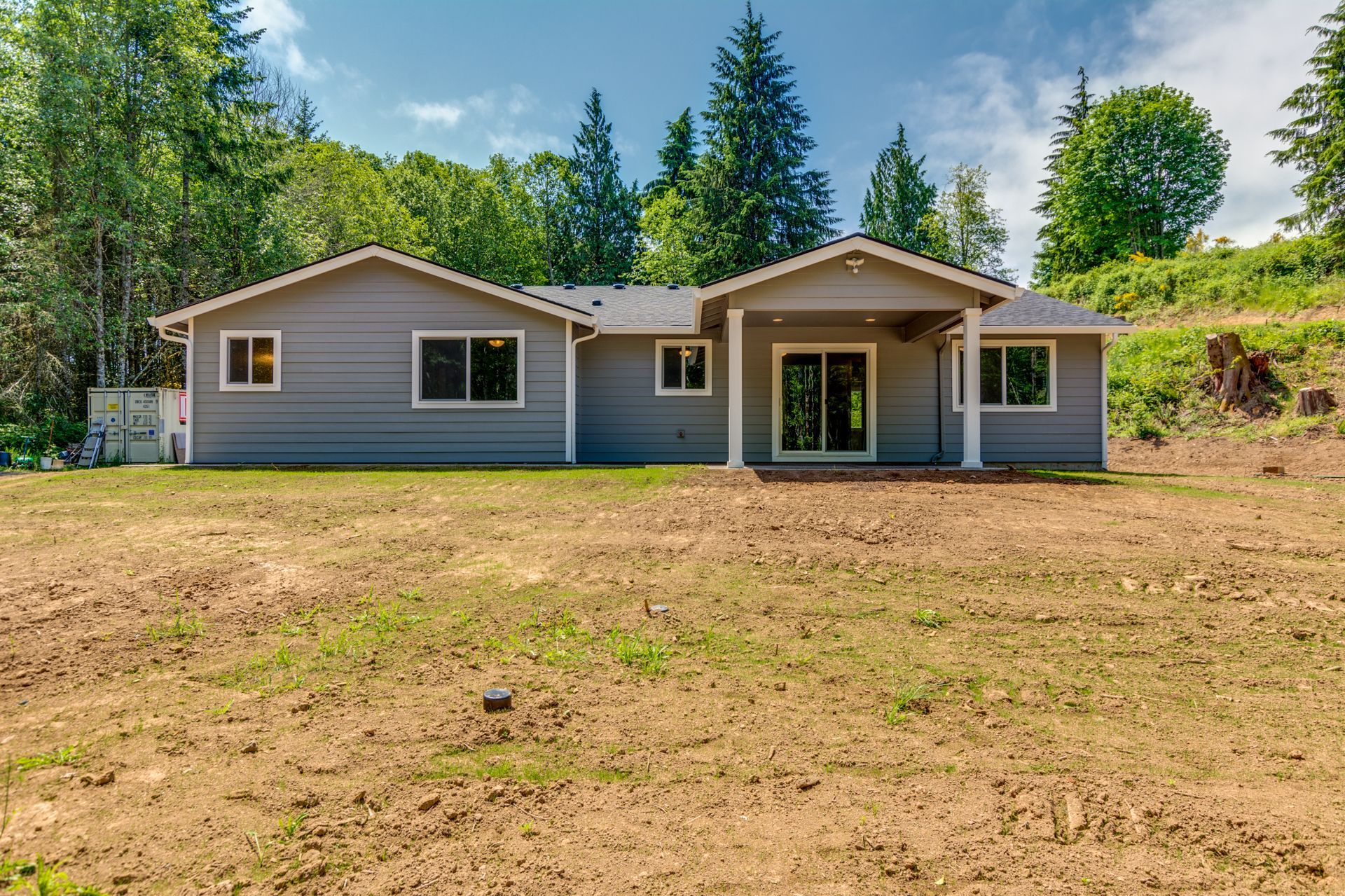 A gray house is sitting in the middle of a grassy field.