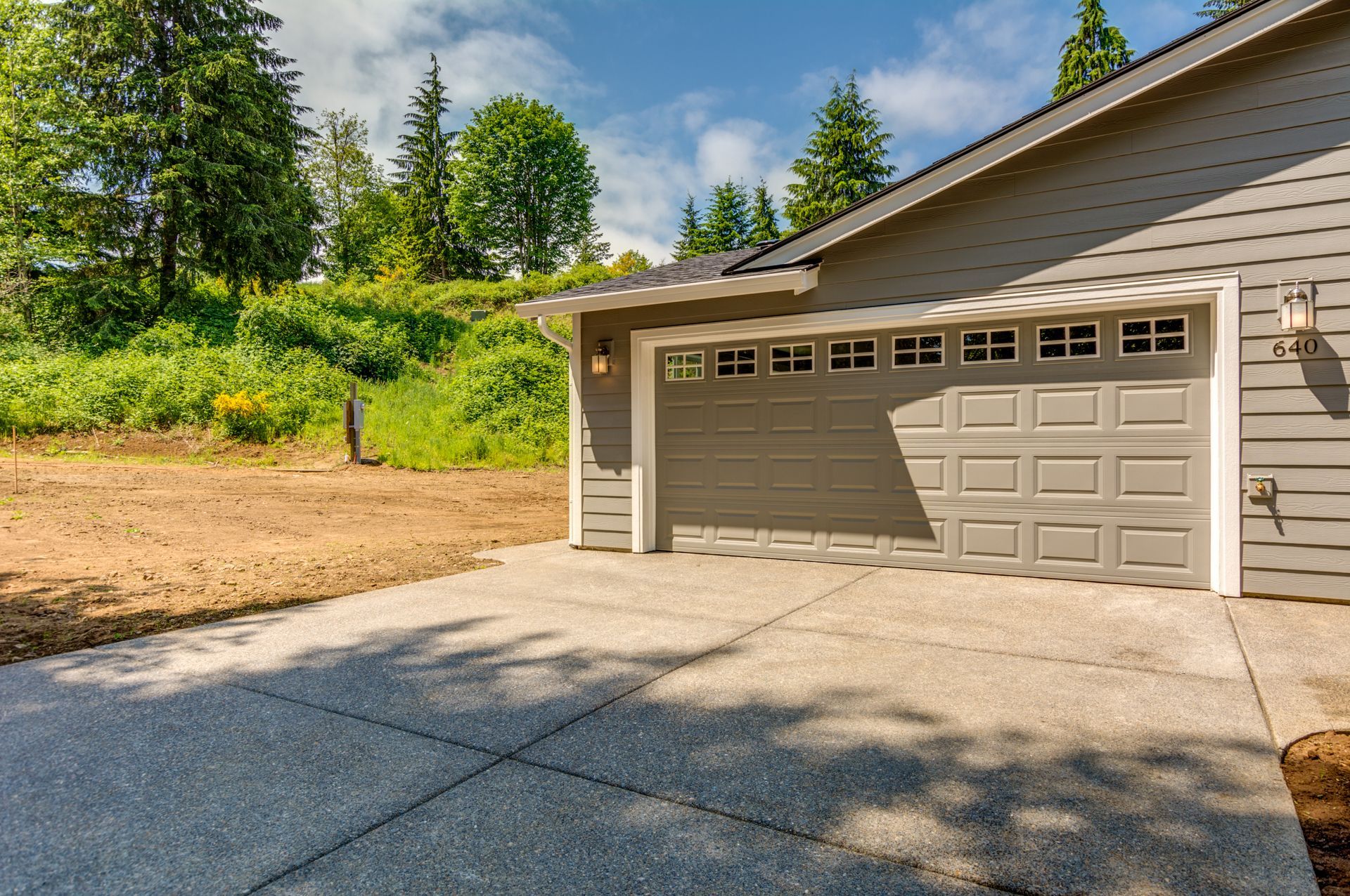 A garage door is open in front of a house with trees in the background.