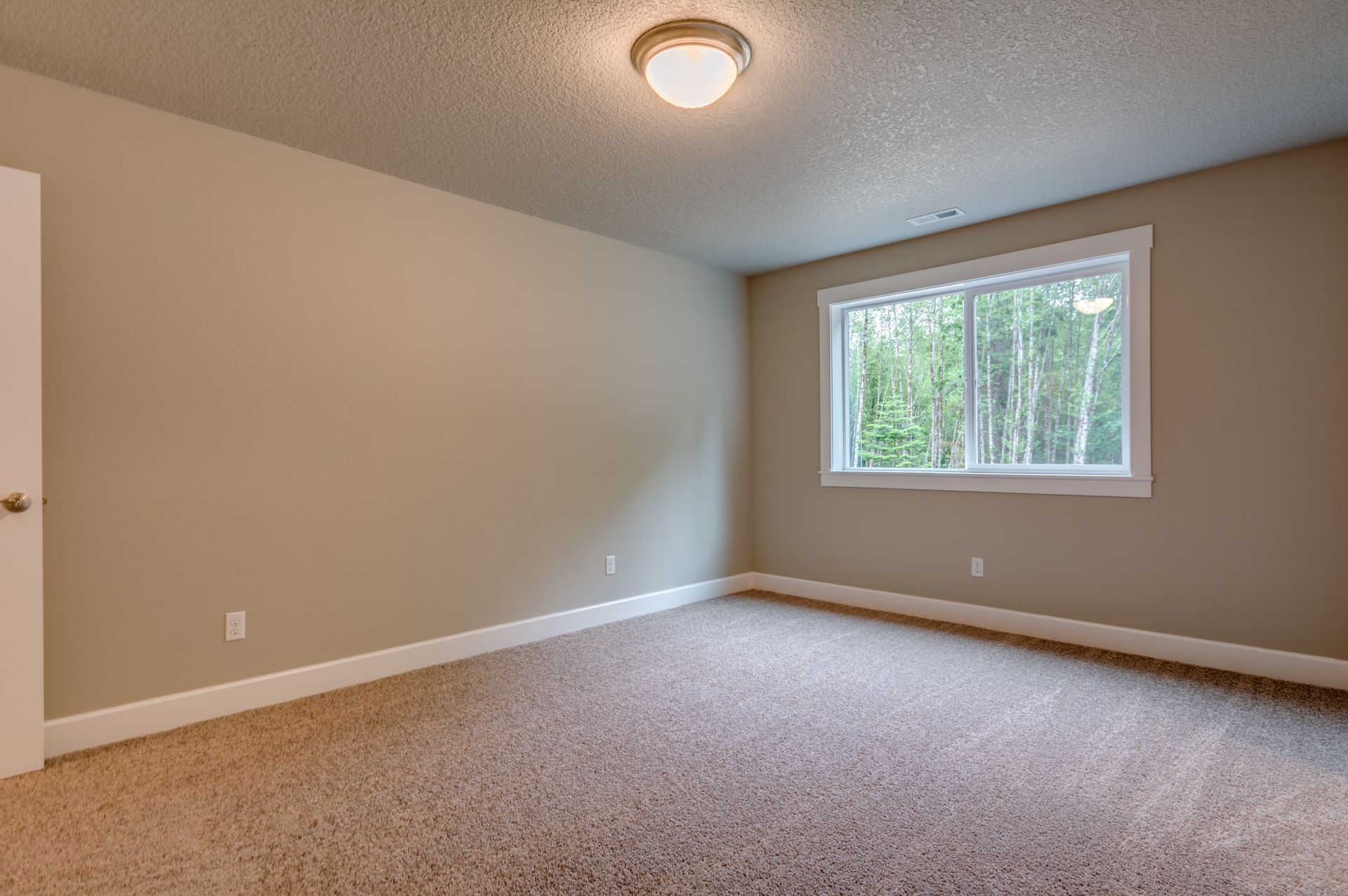 An empty bedroom with a window and a carpeted floor.