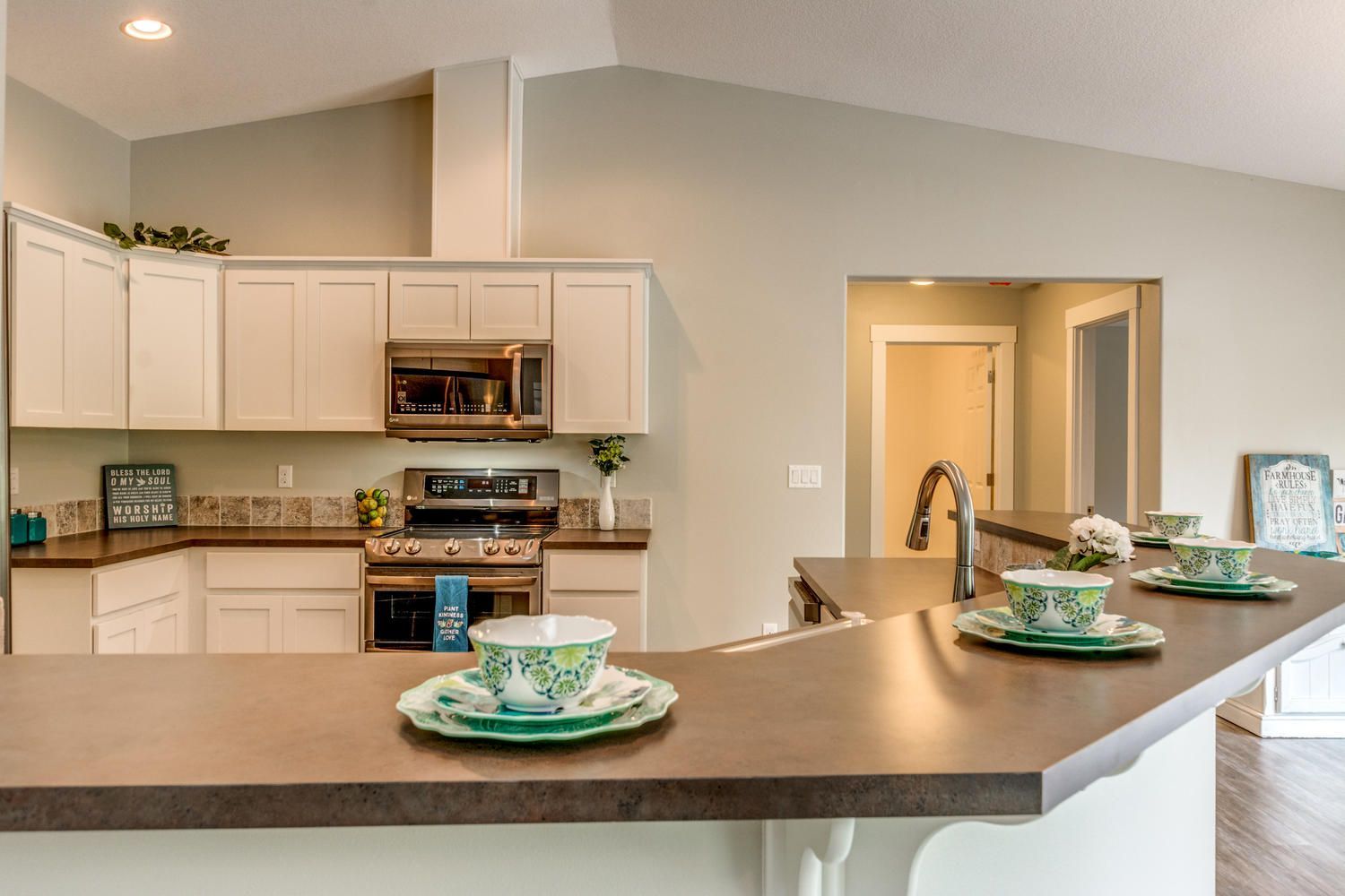 A kitchen with white cabinets , stainless steel appliances , and a counter with plates and cups on it.