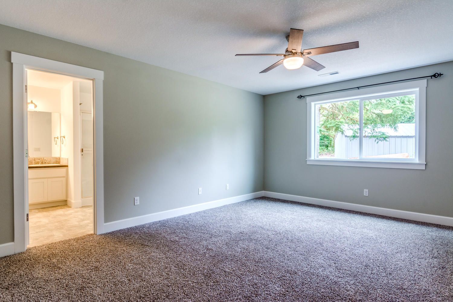 An empty bedroom with a ceiling fan and a window.