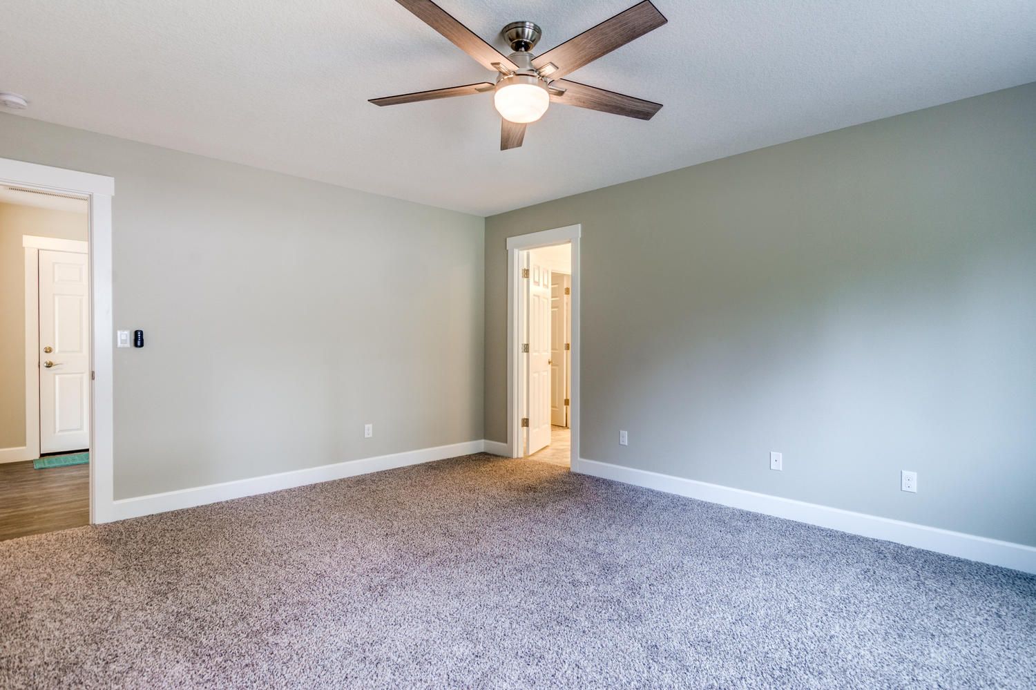 An empty bedroom with a ceiling fan and a carpeted floor.