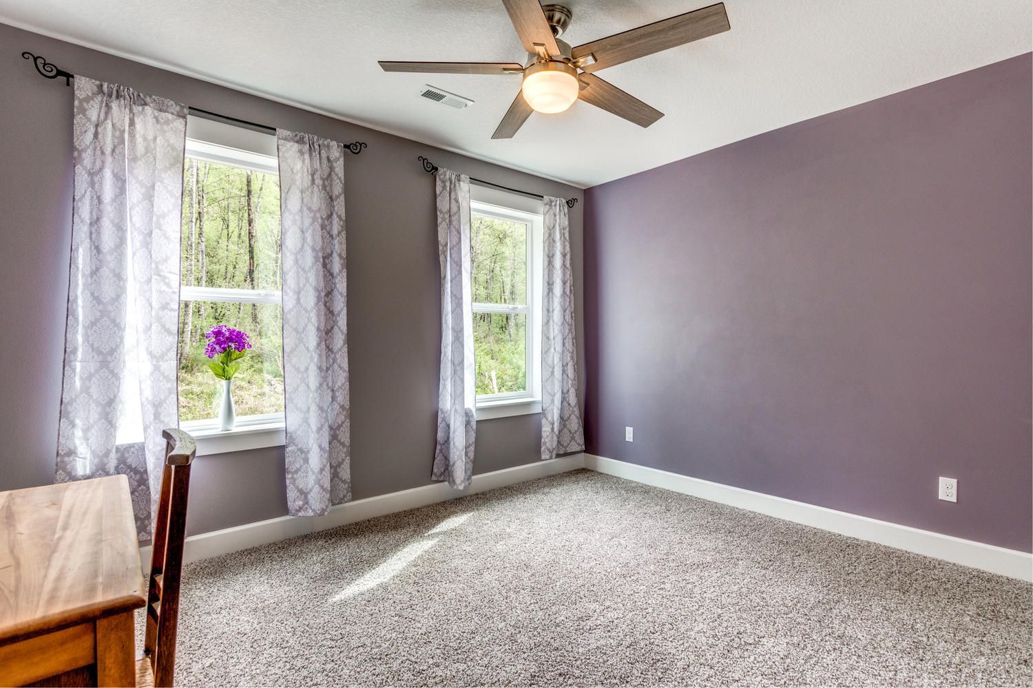 An empty bedroom with purple walls and a ceiling fan.