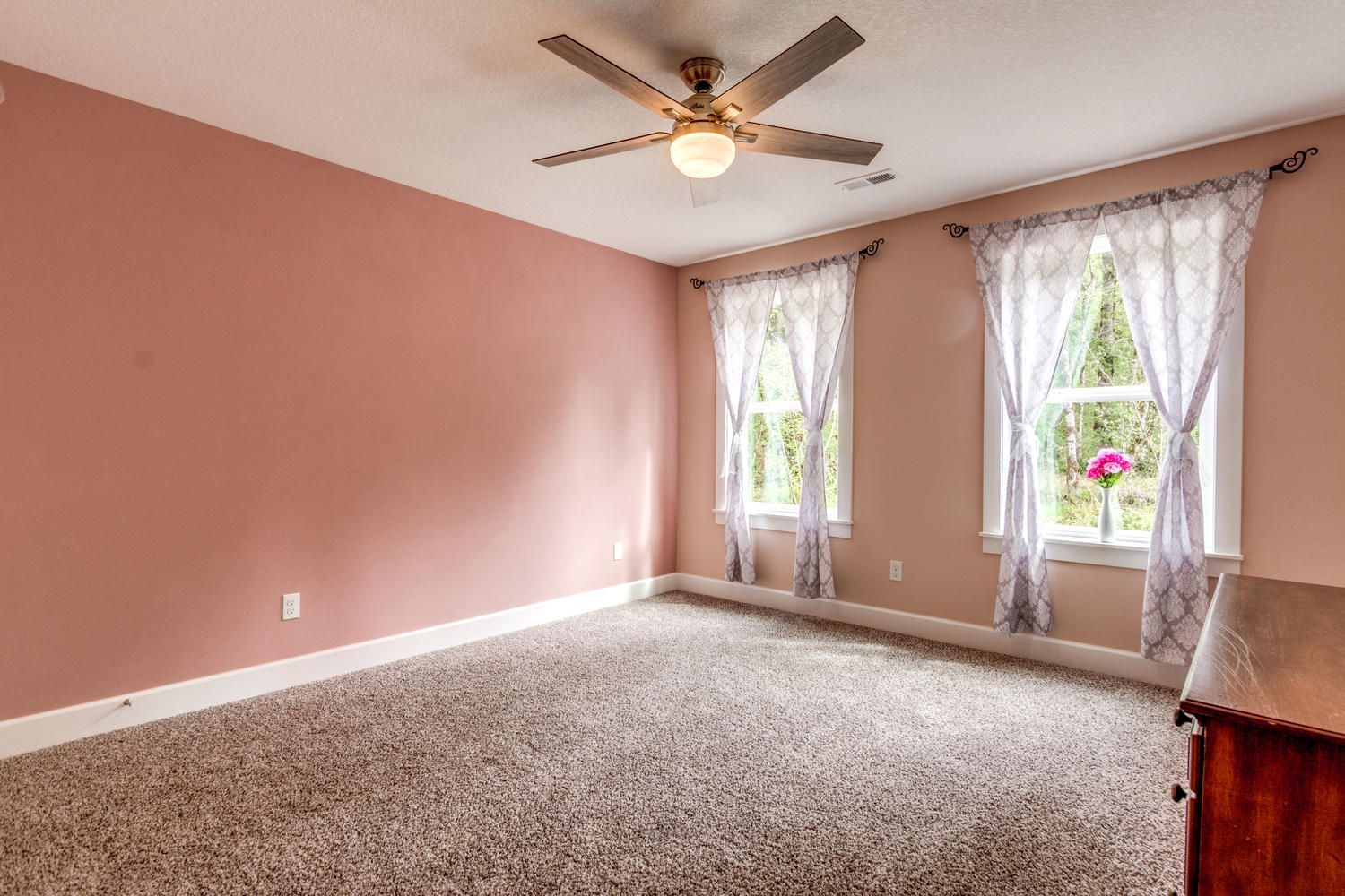 An empty bedroom with pink walls and a ceiling fan.