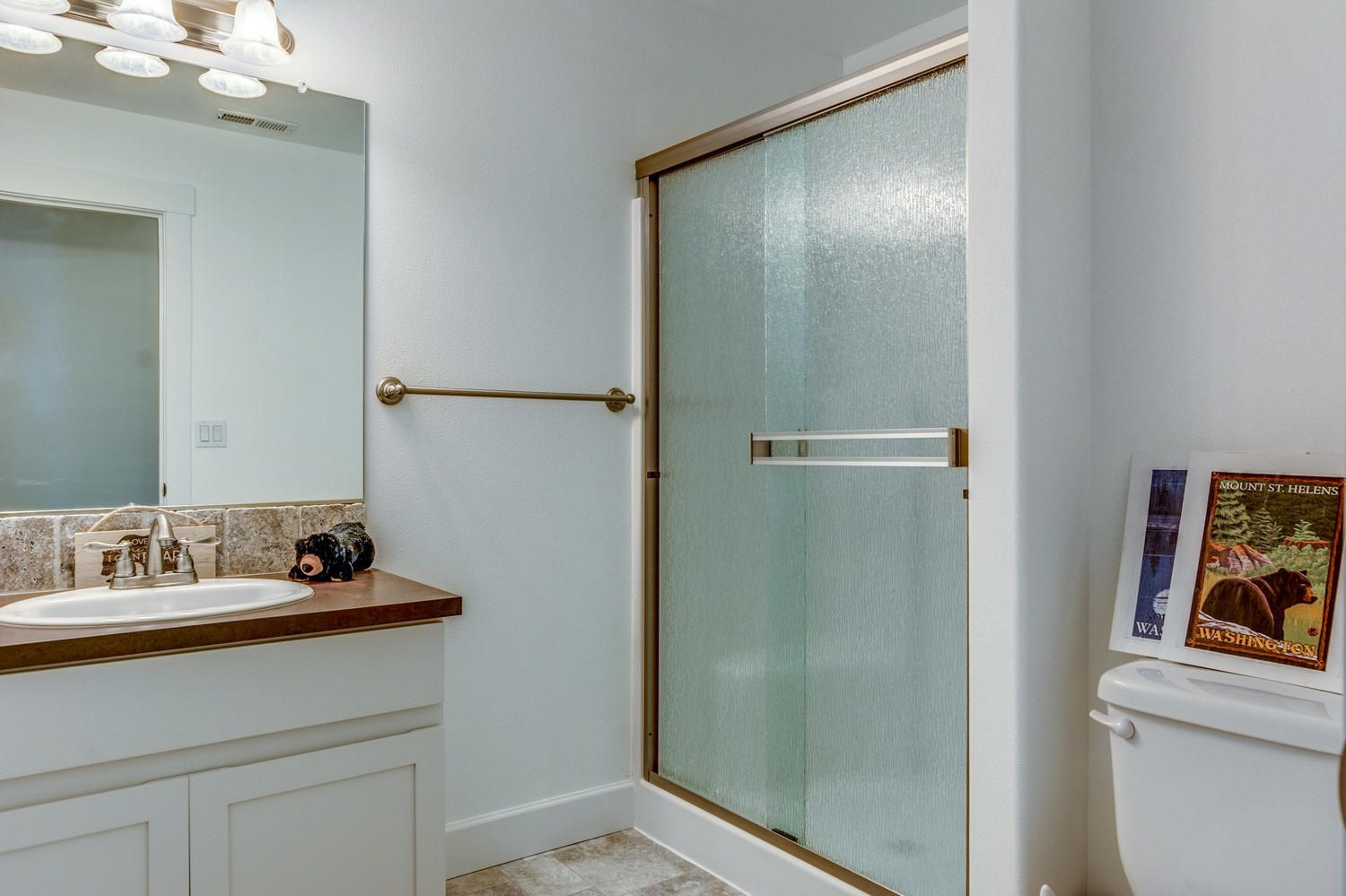 A bathroom with a toilet , sink , mirror and shower.