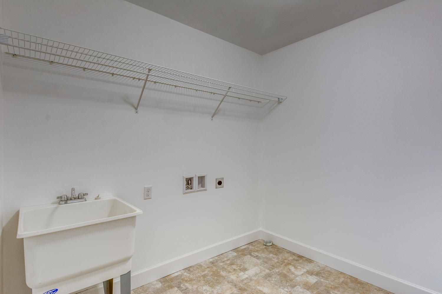 A laundry room with a sink and shelves on the wall.