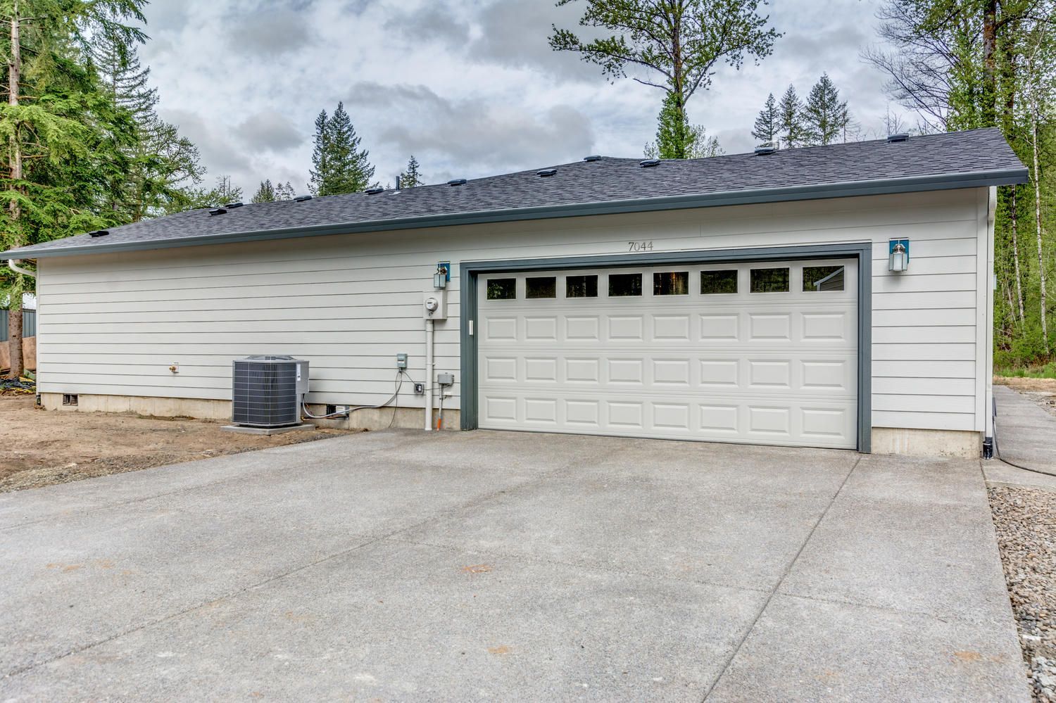 A white garage with a black roof and a concrete driveway