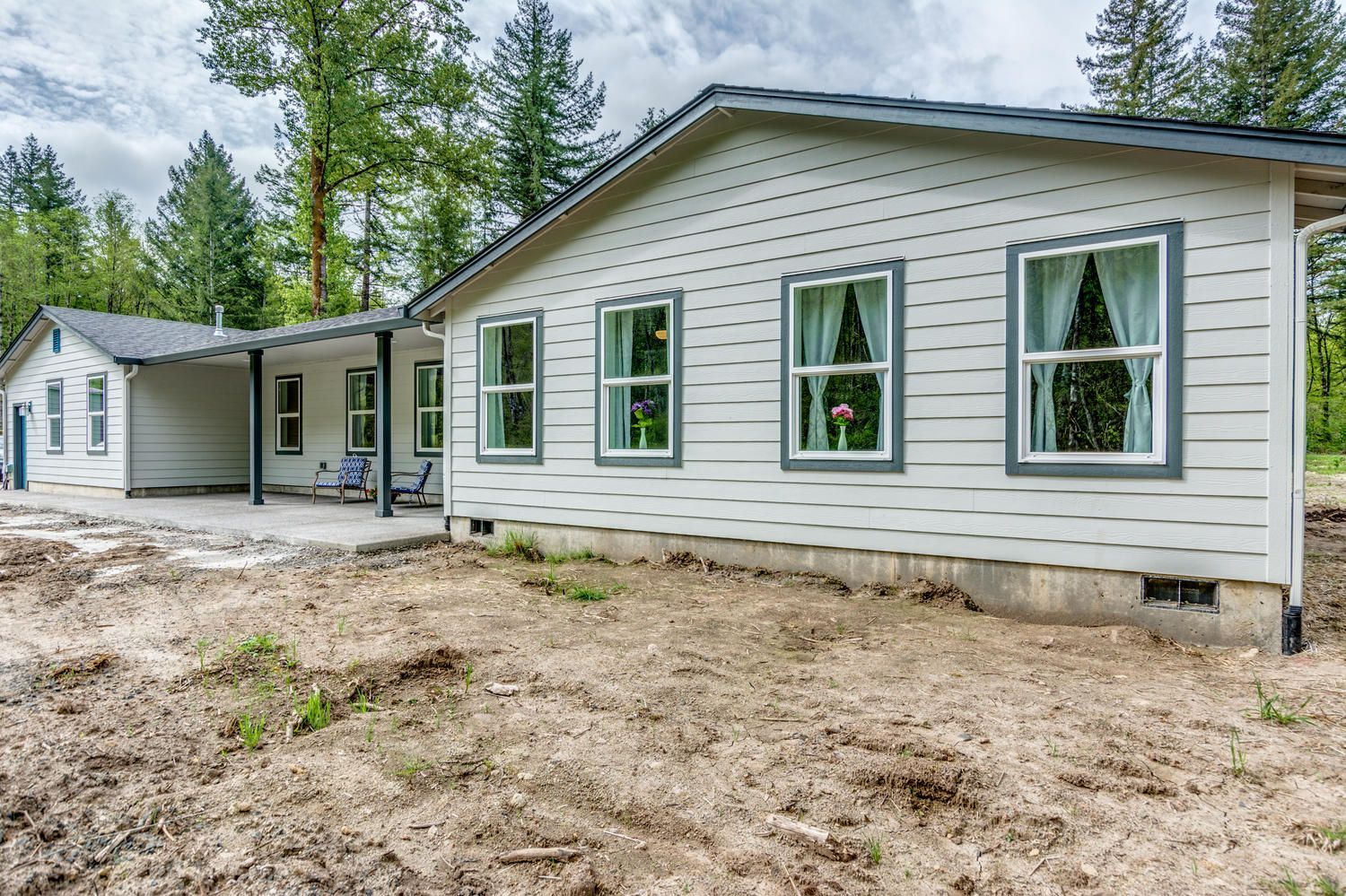 A white house with a porch is sitting in the middle of a dirt field.