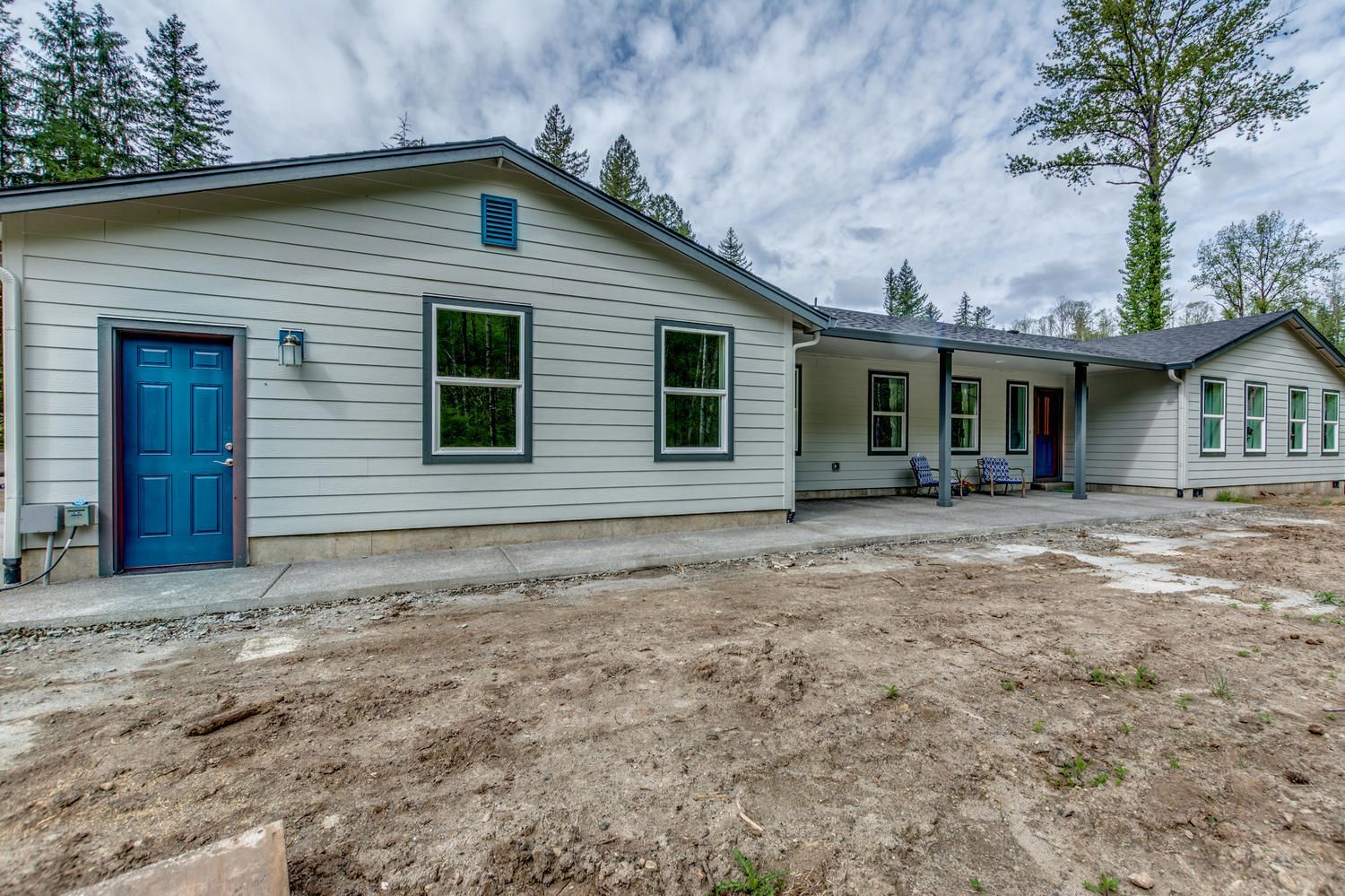 A white house with a blue door is sitting in the middle of a dirt field.