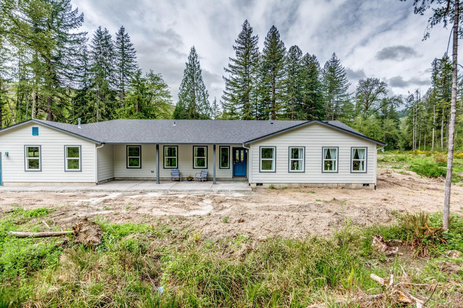 A large white house with a blue door is surrounded by trees