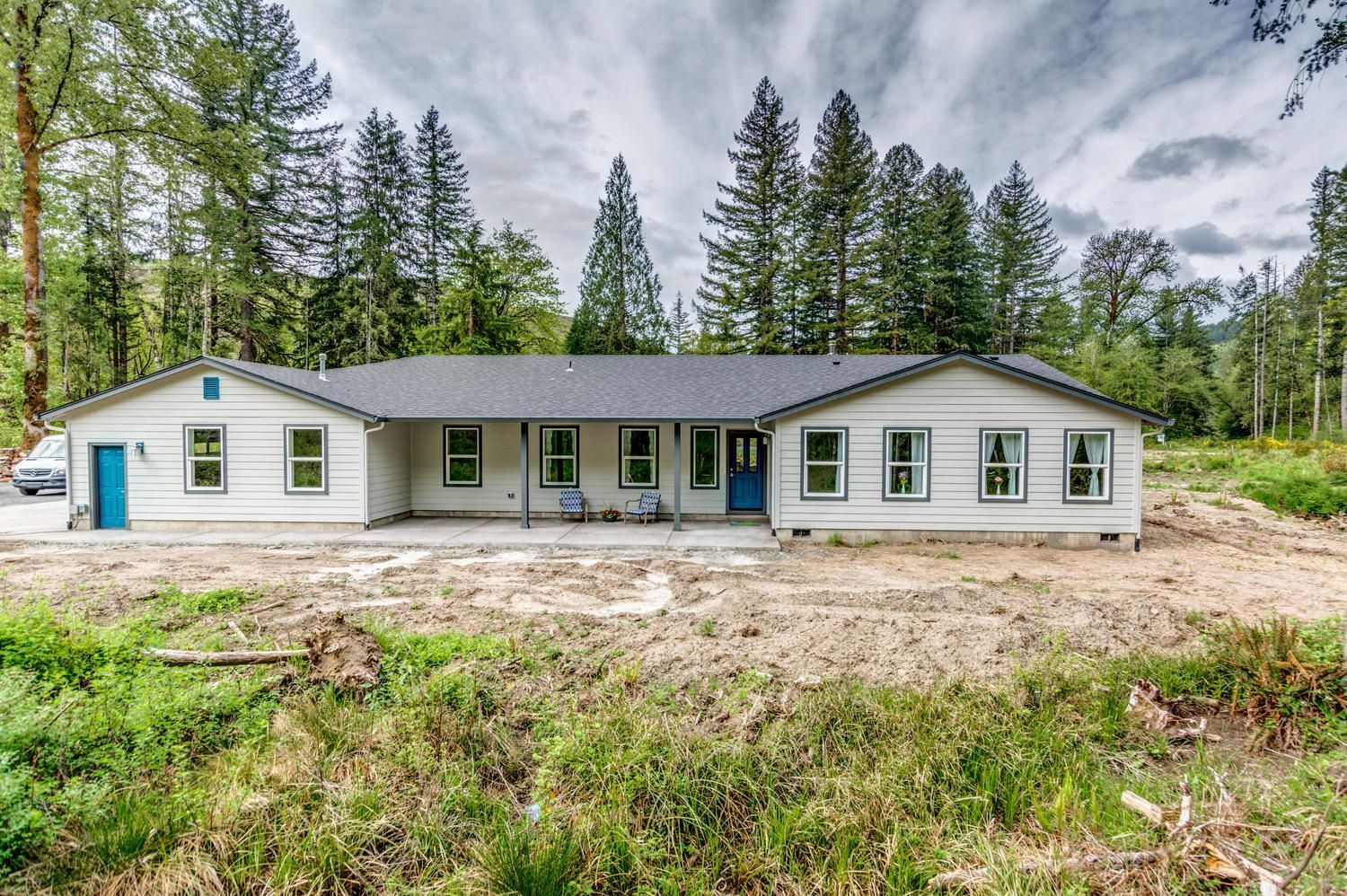 A large white house with a blue door is surrounded by trees.