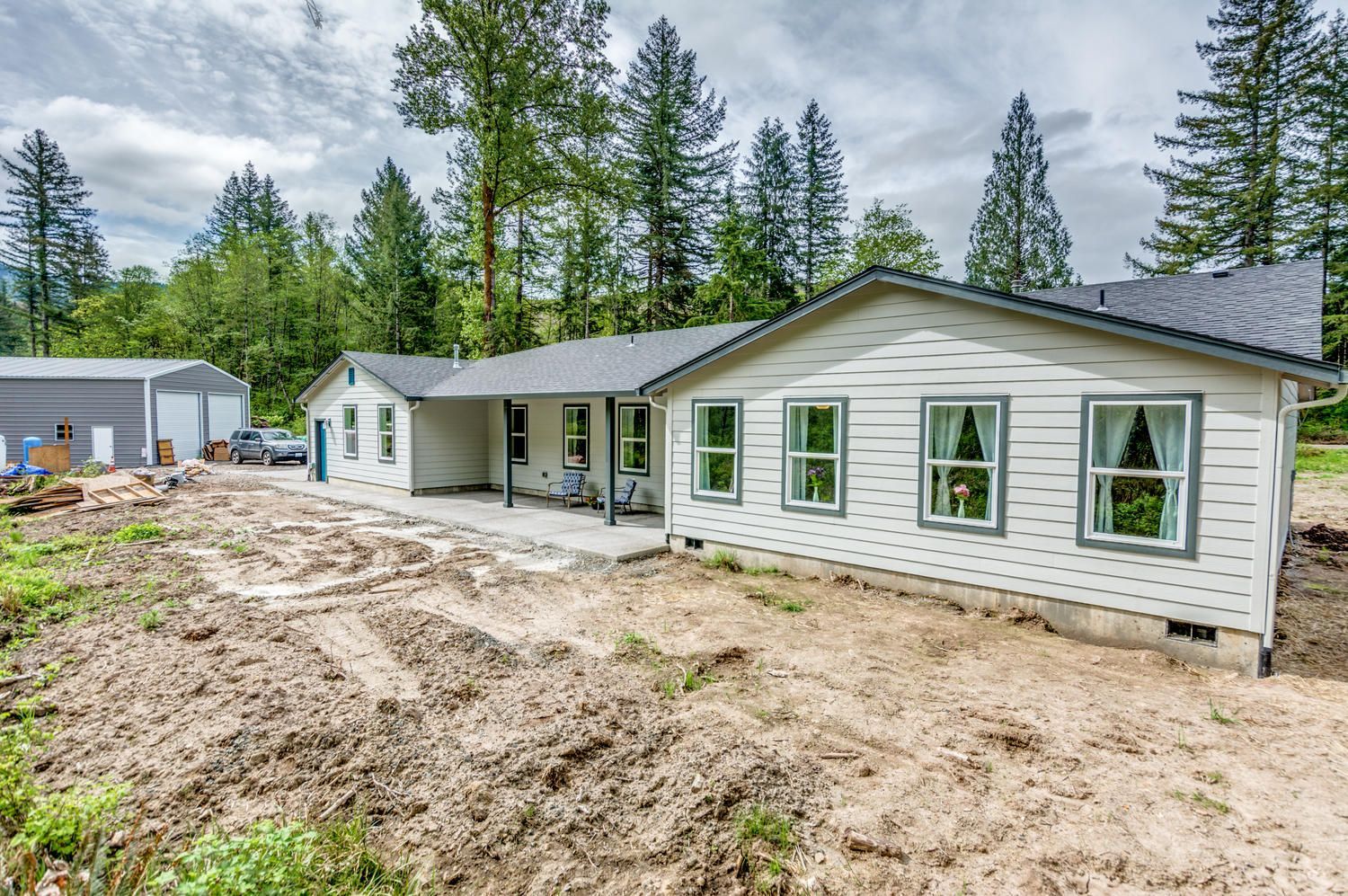 A white house is sitting in the middle of a dirt field surrounded by trees.