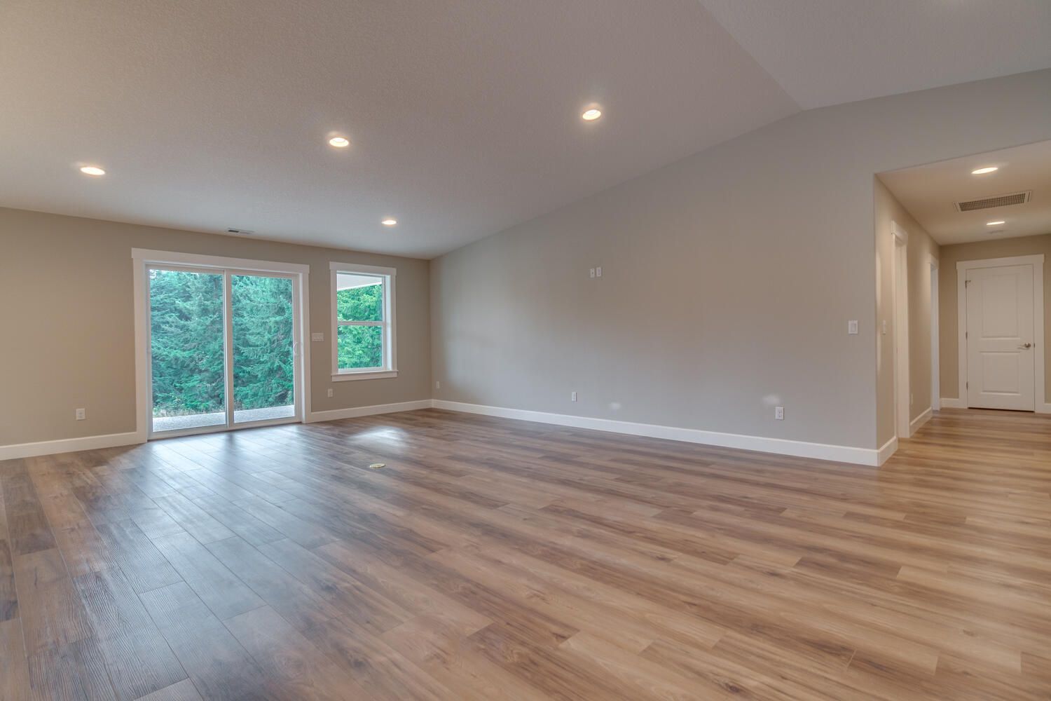 An empty living room with hardwood floors and sliding glass doors.