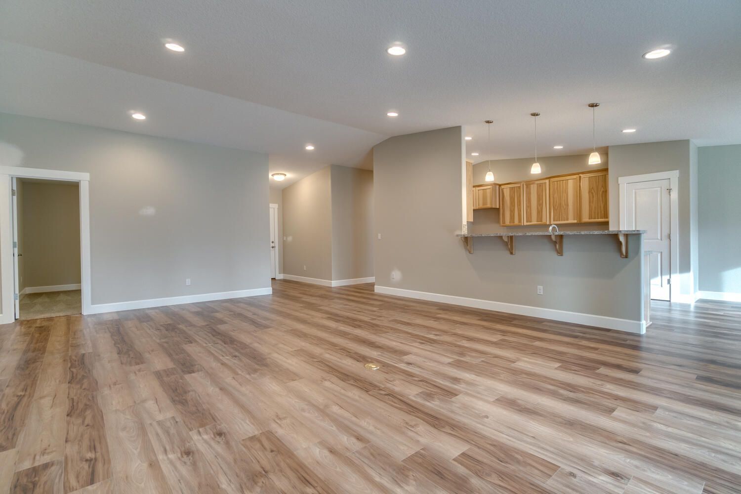 An empty living room with hardwood floors and a kitchen in the background.
