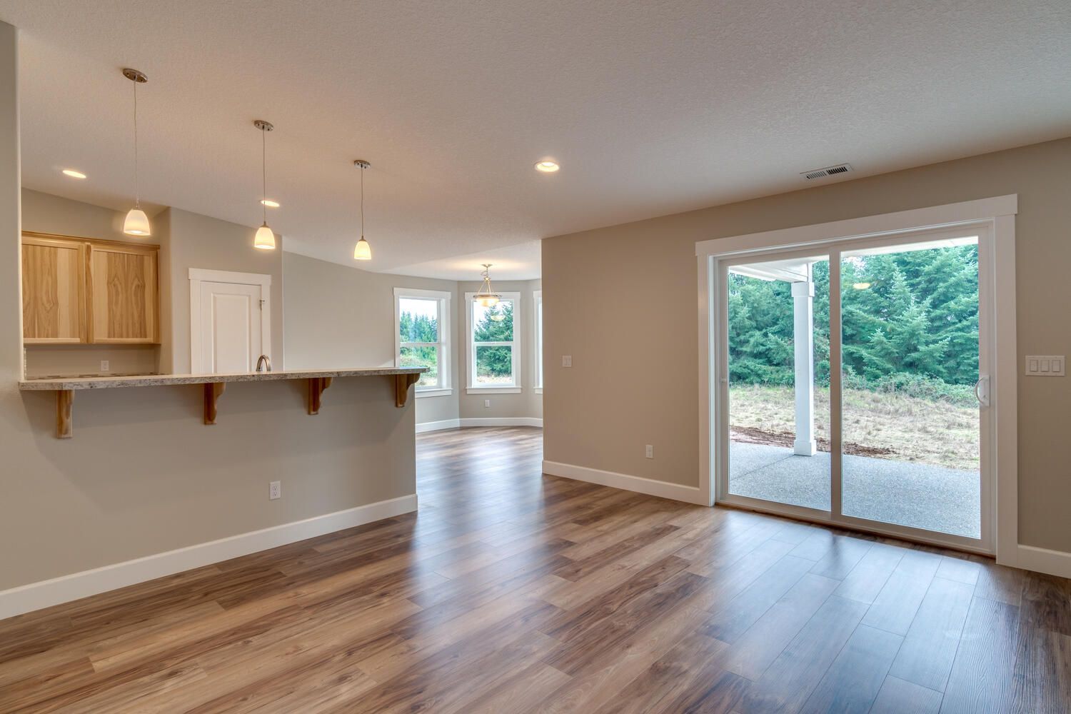 An empty living room with hardwood floors and sliding glass doors leading to a patio.