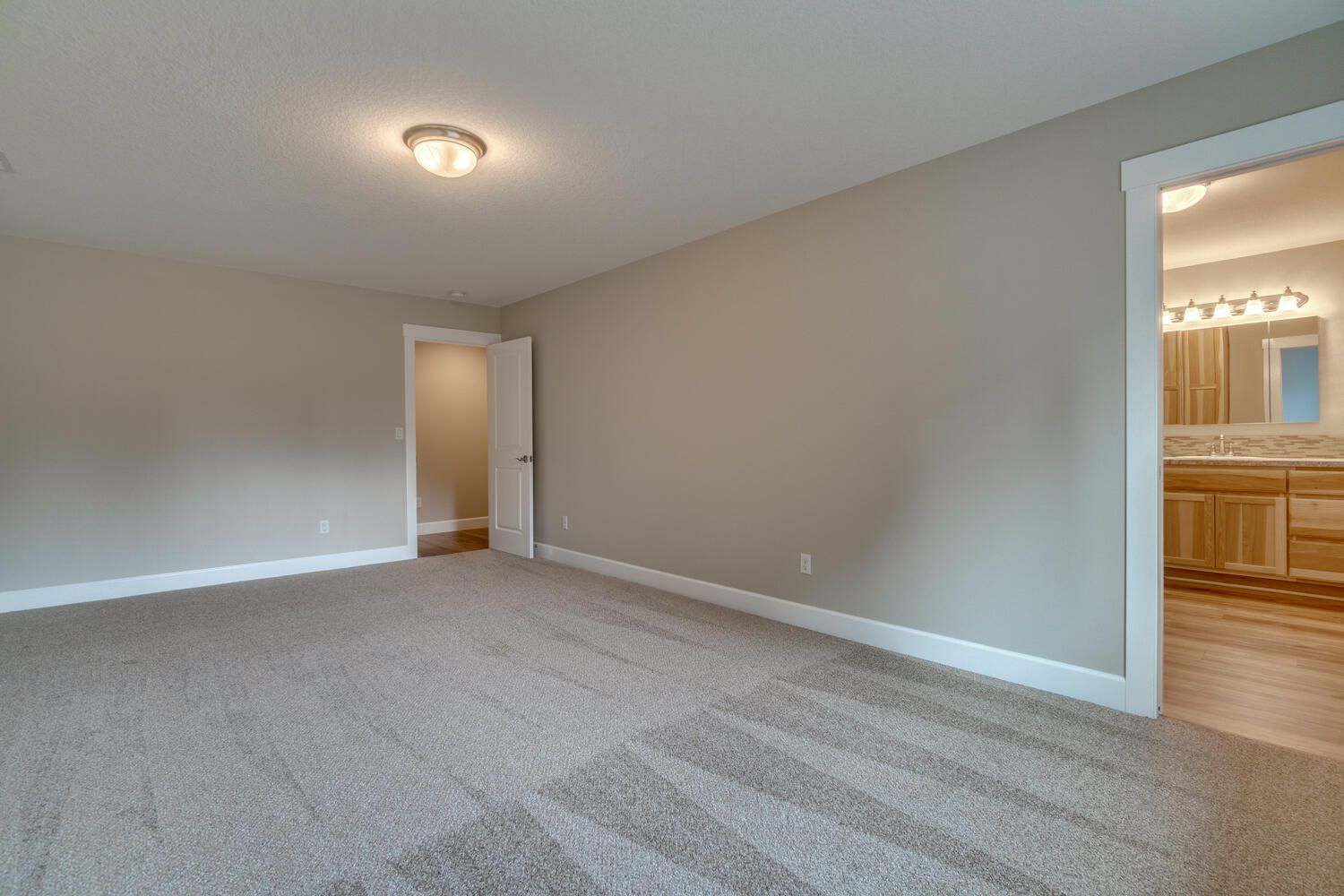 An empty bedroom with a carpeted floor and a bathroom in the background.