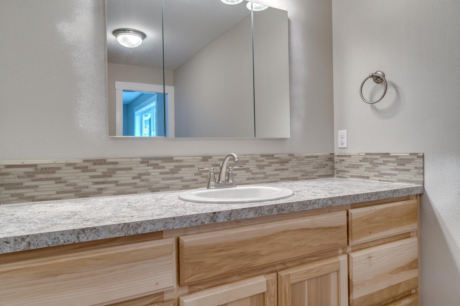 A bathroom with a sink , mirror and wooden cabinets.