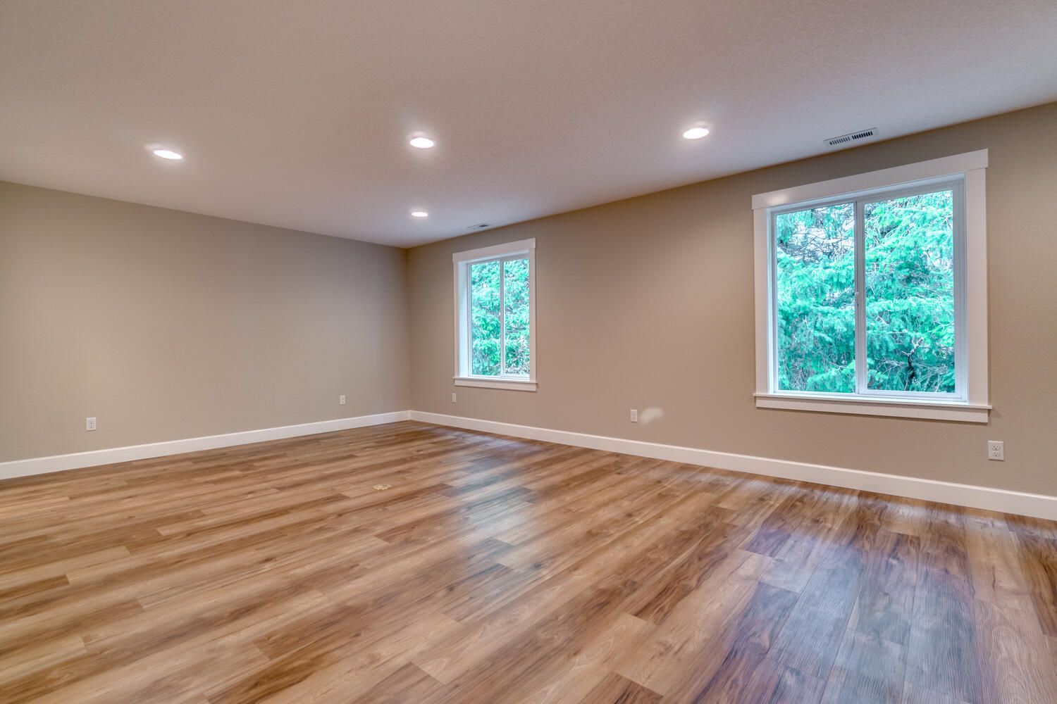 An empty room with hardwood floors and two windows.