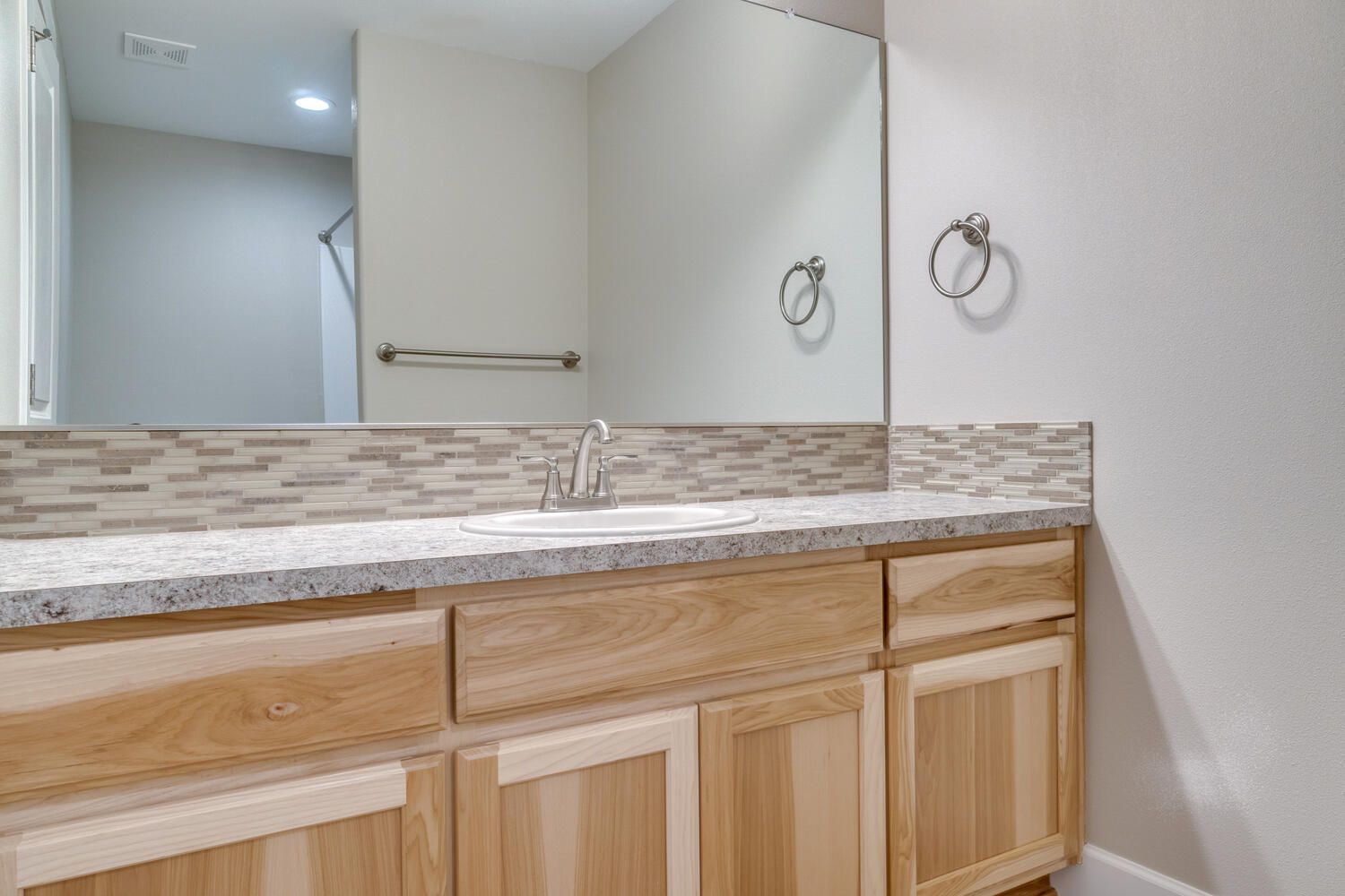 A bathroom with a sink , mirror and wooden cabinets.