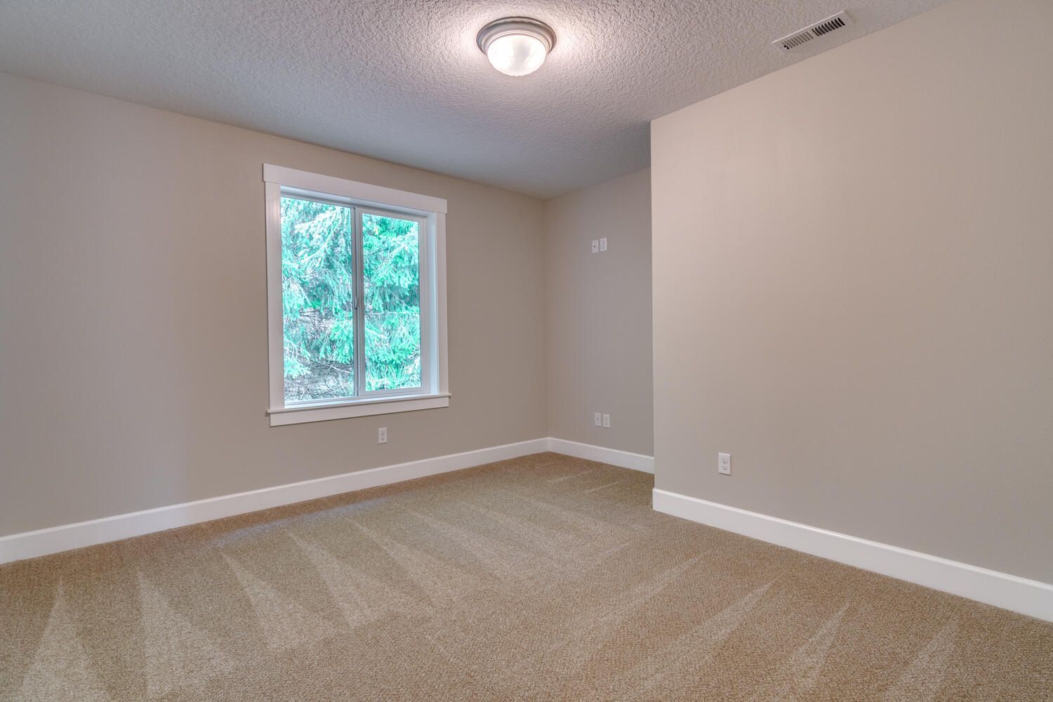 An empty bedroom with a window and a carpeted floor.