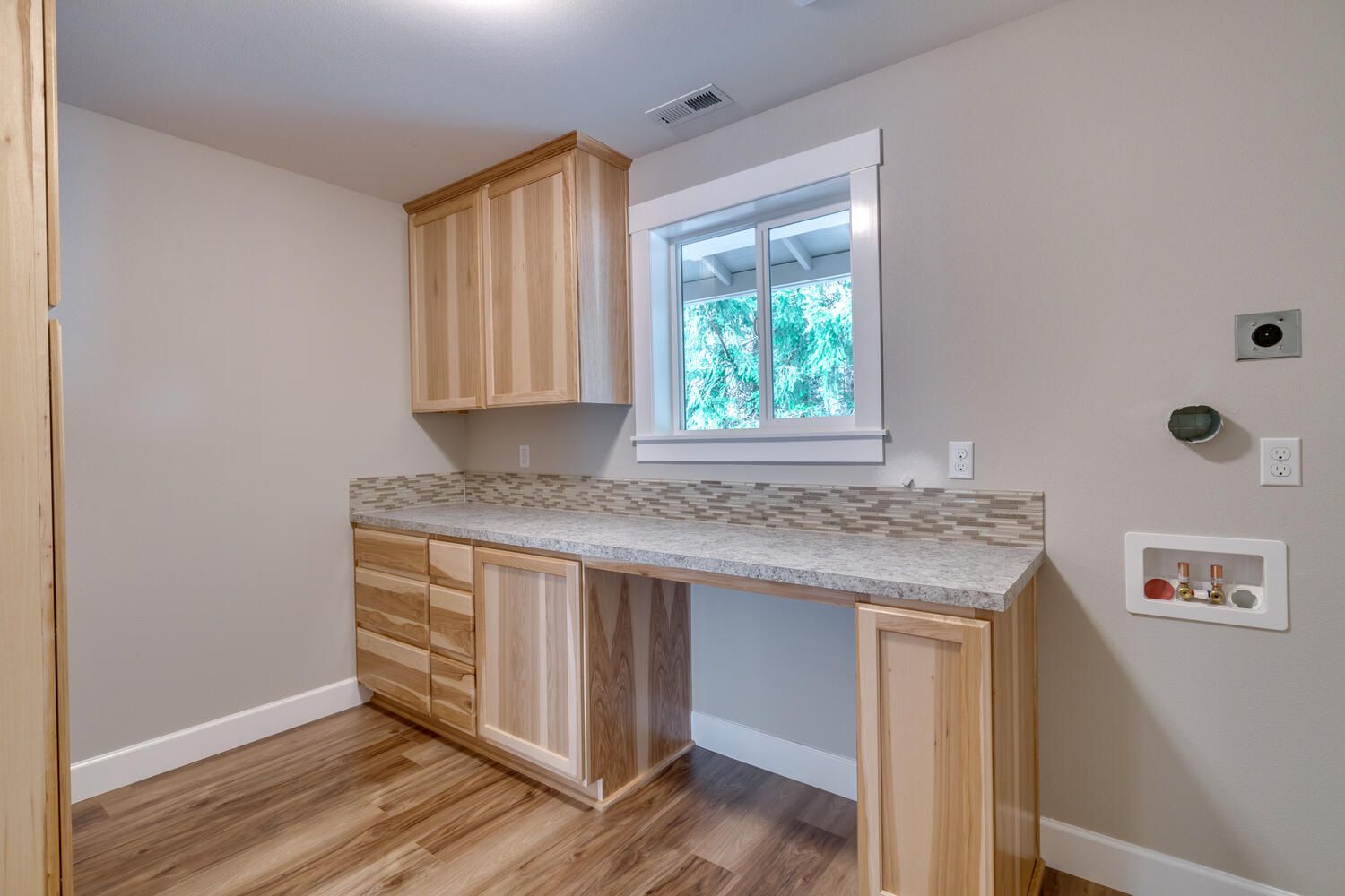 A laundry room with wooden cabinets , granite counter tops , and a window.