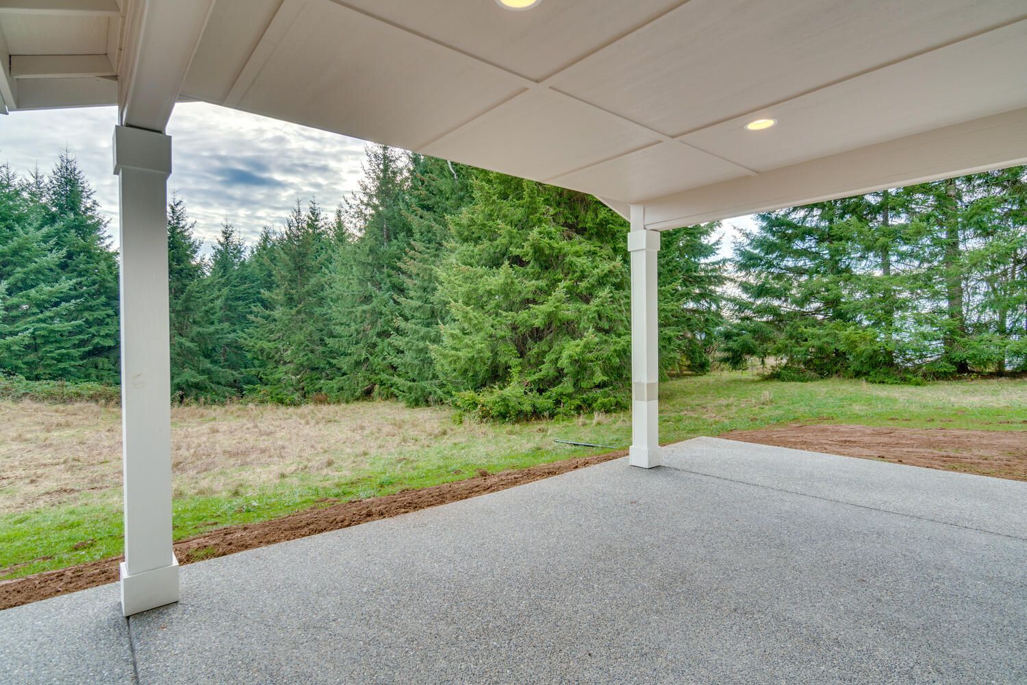 A covered patio with a view of a field and trees.