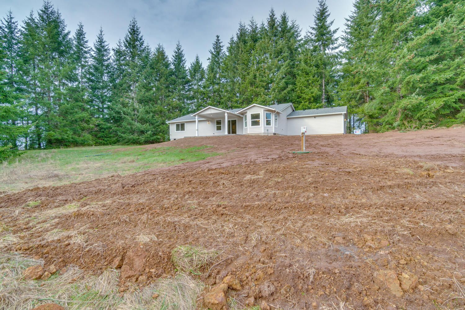 A white house sits on top of a dirt hill surrounded by trees