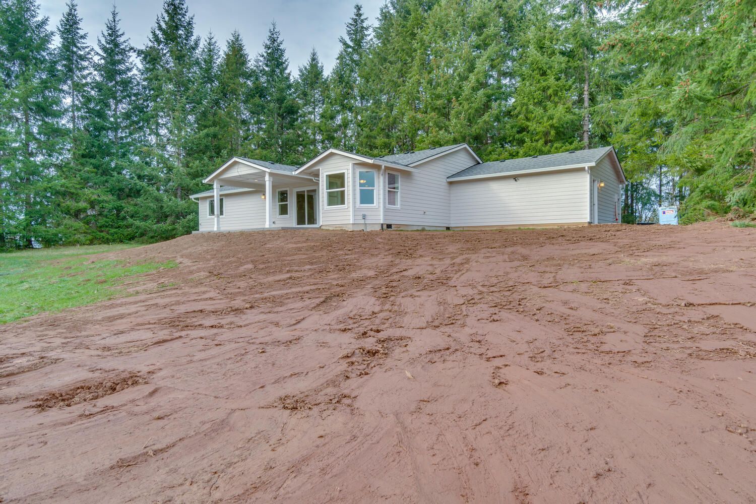 A white house sits on top of a dirt hill surrounded by trees