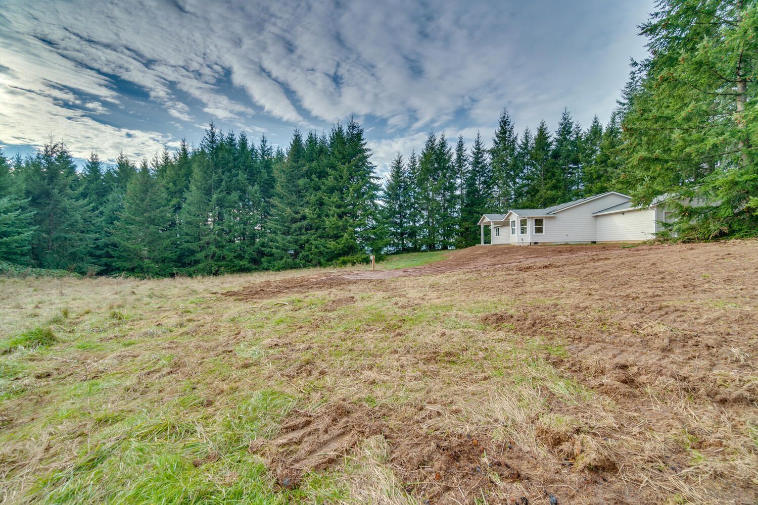 A white house is sitting in the middle of a grassy field surrounded by trees.