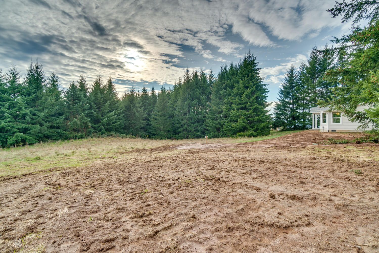 A dirt field with trees in the background and a house in the background