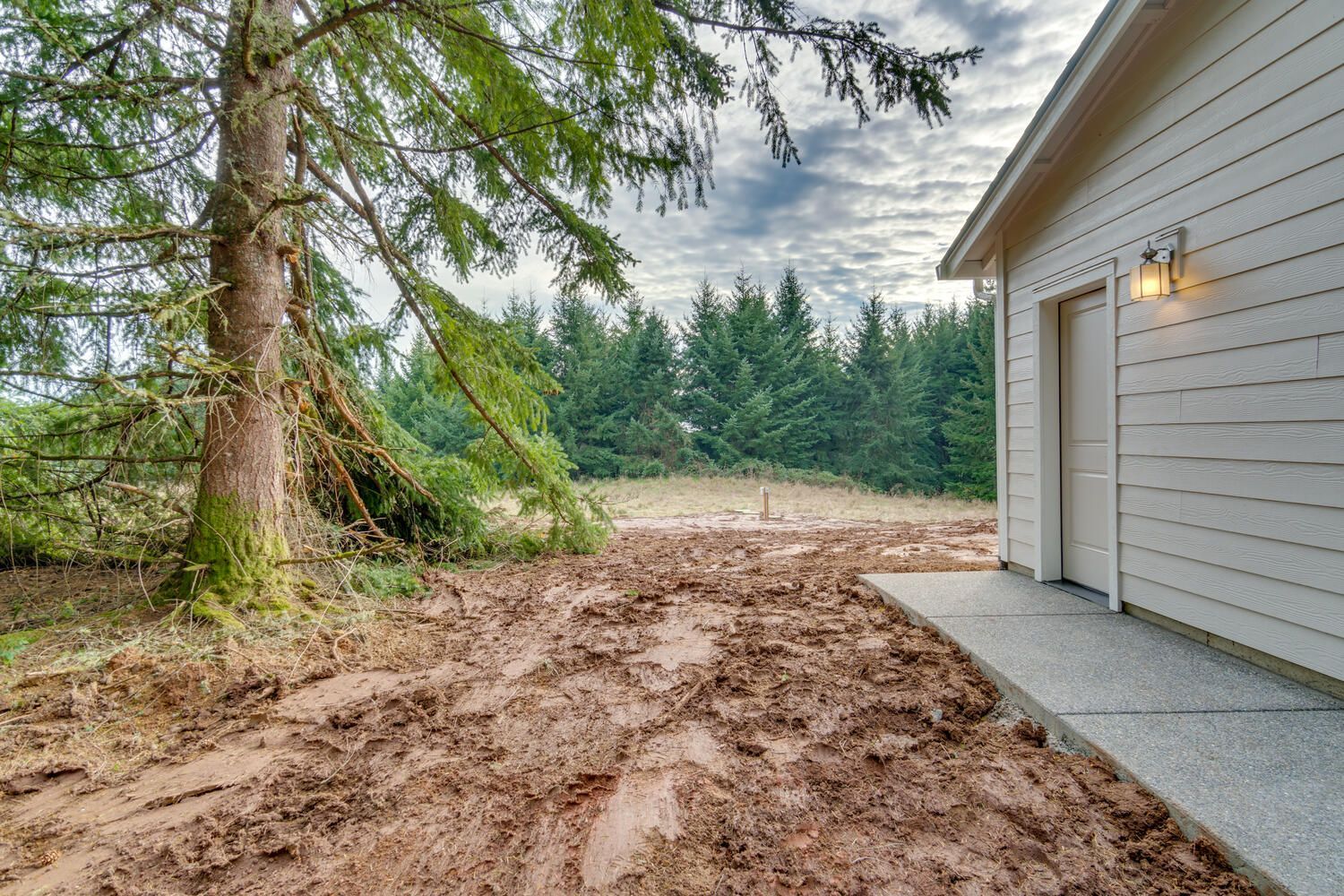 A white garage with a tree in the background and a dirt path leading to it.