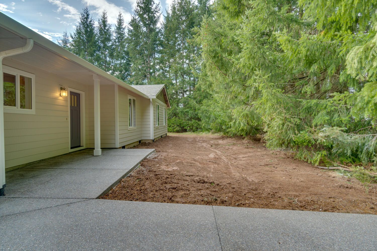 A house with a covered porch and a driveway in front of it surrounded by trees.
