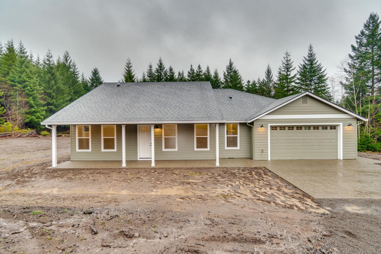A house with a gray roof sits in the middle of a dirt field