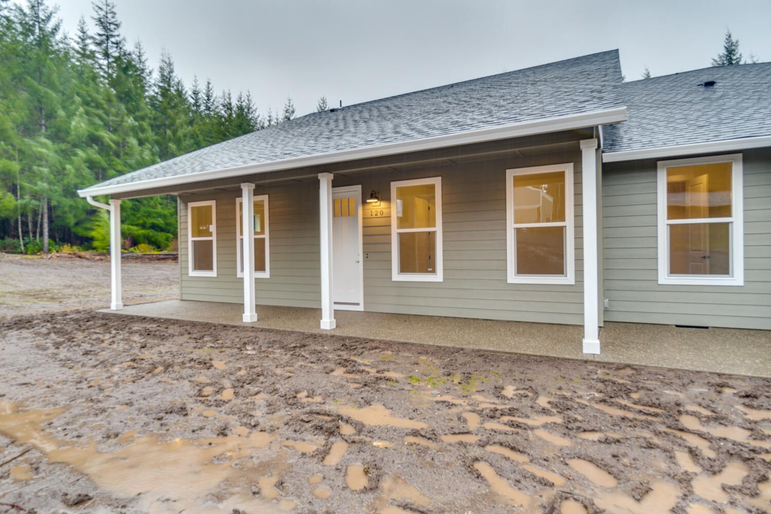 A house with a porch is sitting in the middle of a dirt field.