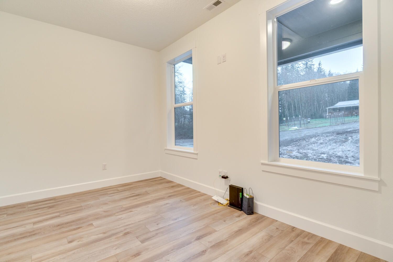 An empty room with hardwood floors and two windows.