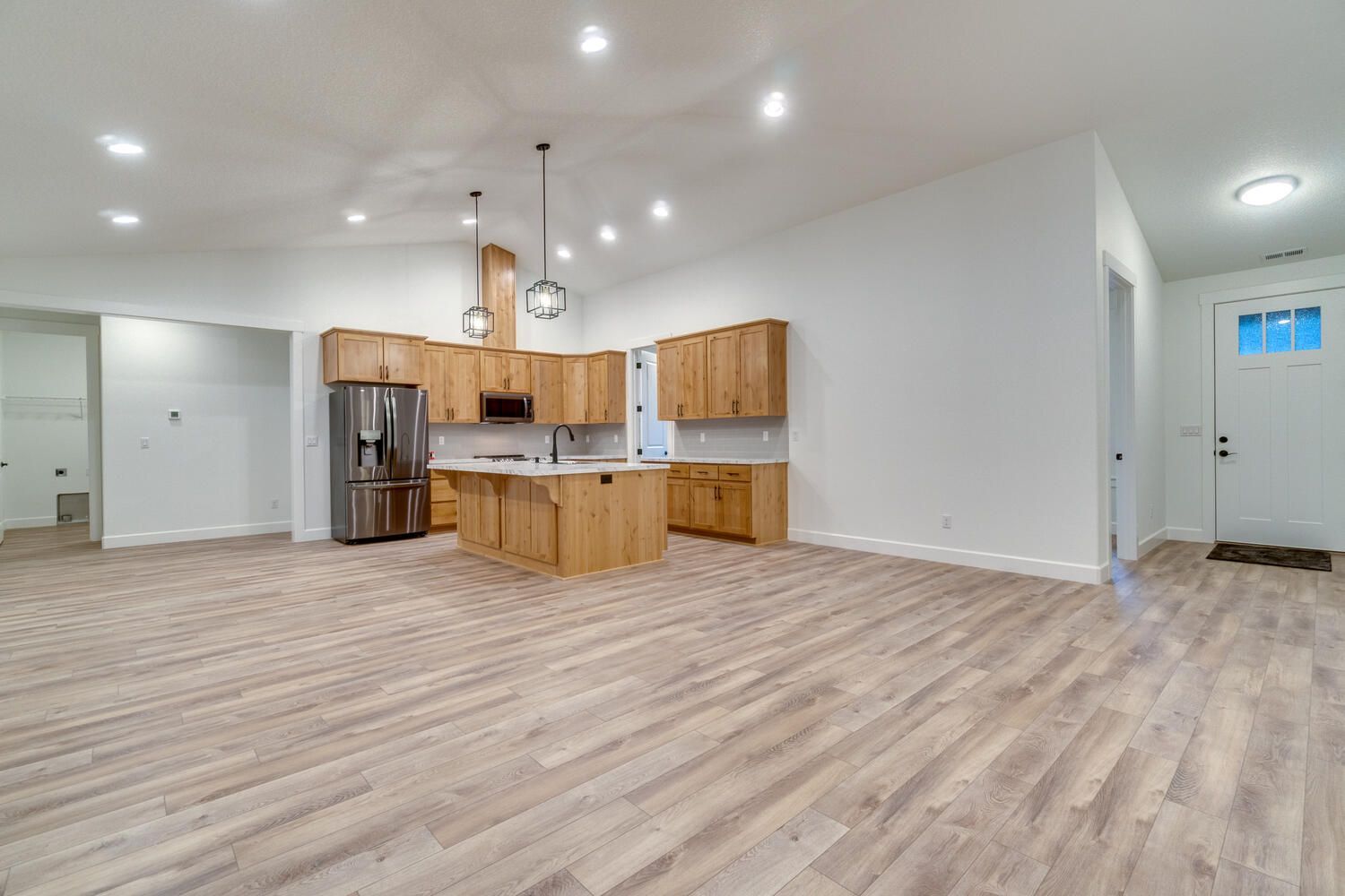 A large empty room with hardwood floors and a kitchen.