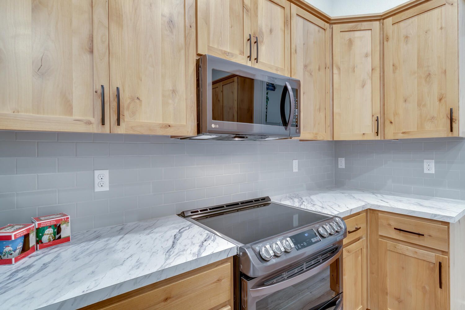 A kitchen with wooden cabinets , a stove , microwave , and marble counter tops.
