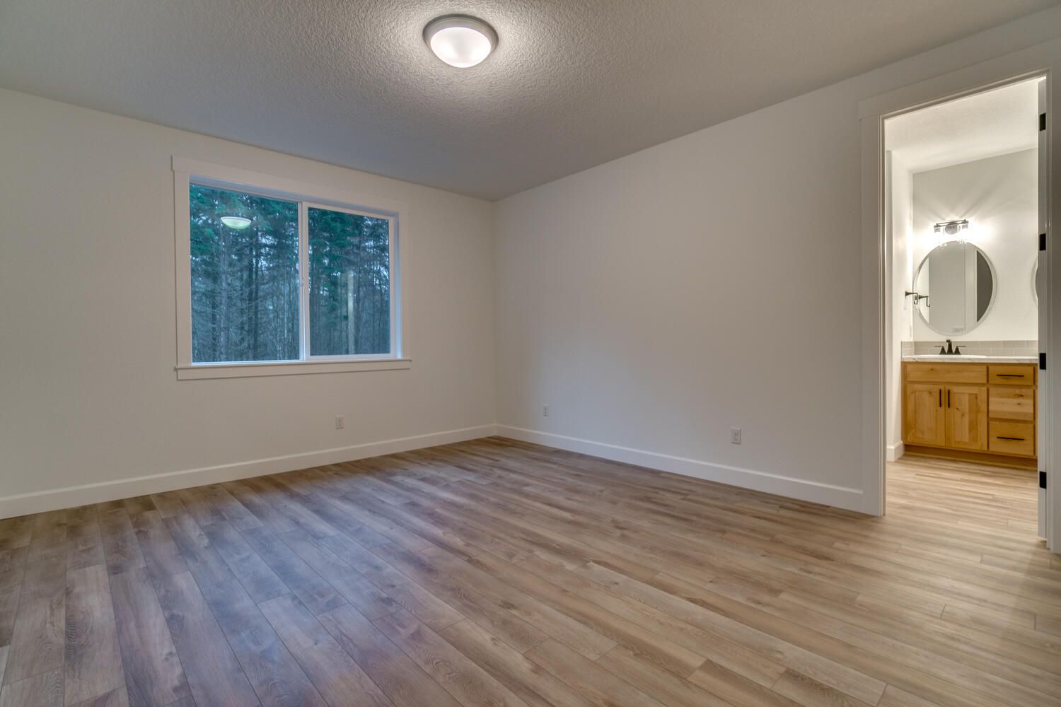 An empty bedroom with hardwood floors and a bathroom.